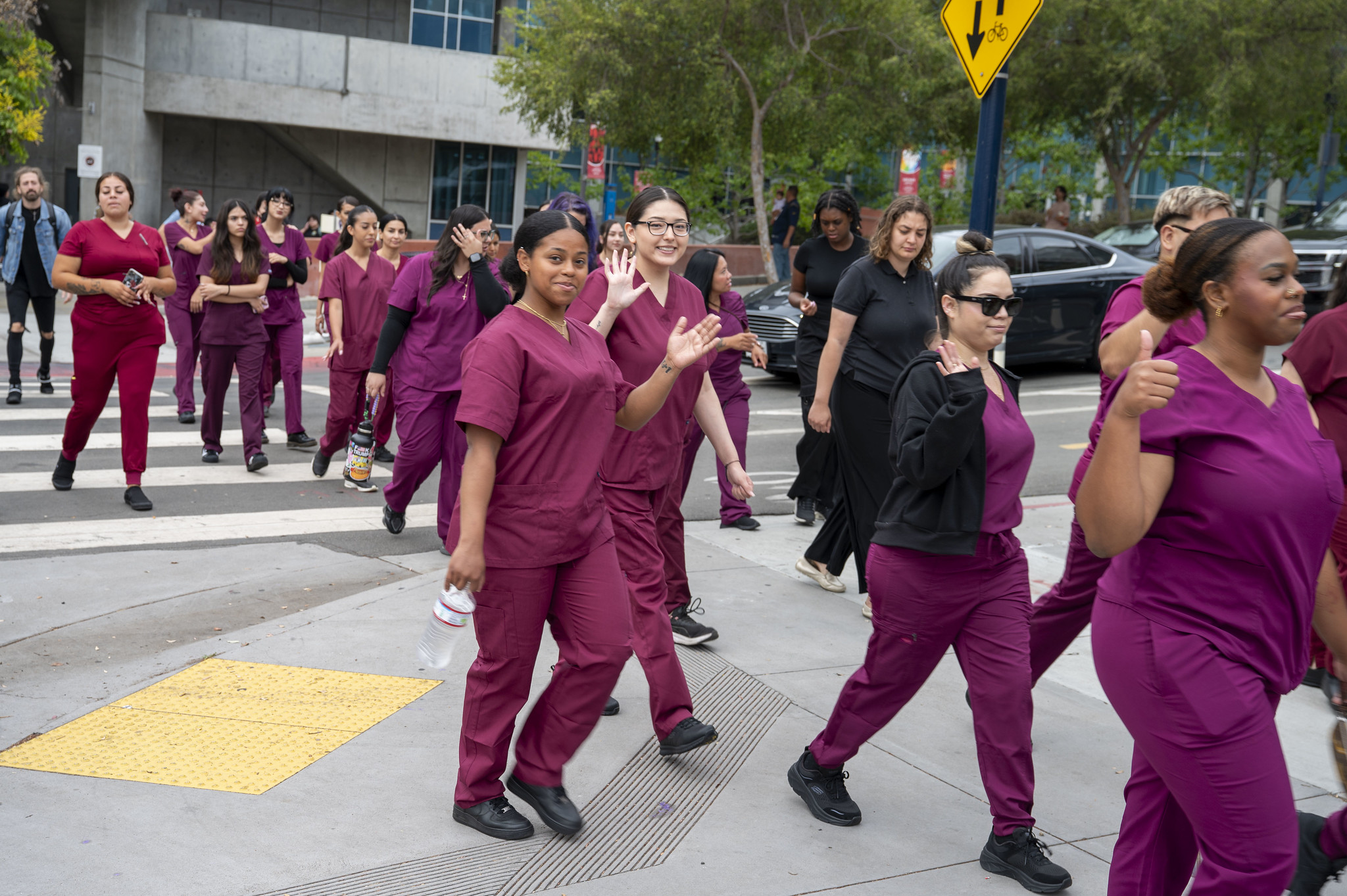 
A group of nail technology students in maroon scrubs cross the street at City College.
