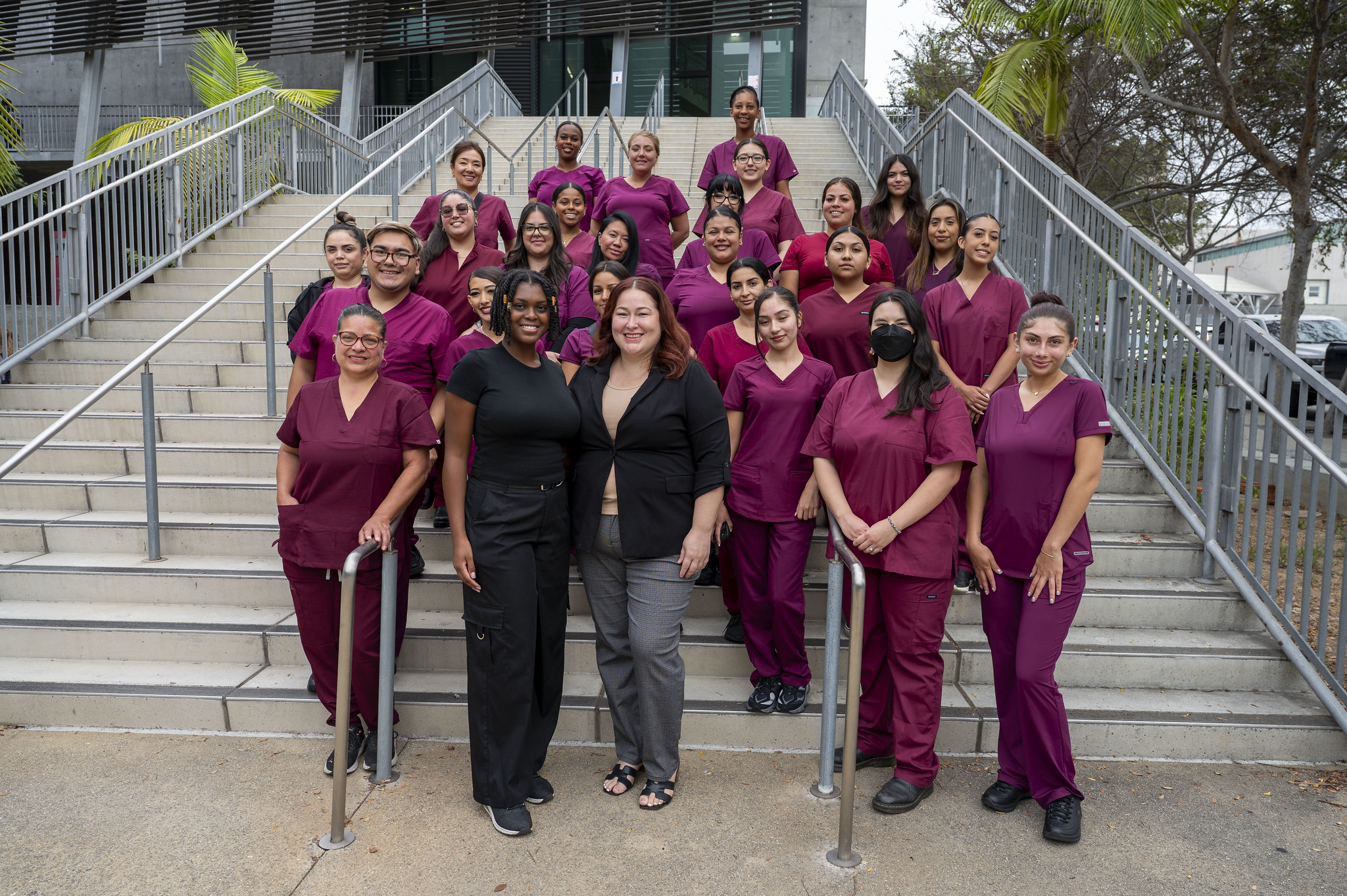 
Nail technology students in maroon scrubs take a group photo on stairs outside of a City College building.&nbsp;
