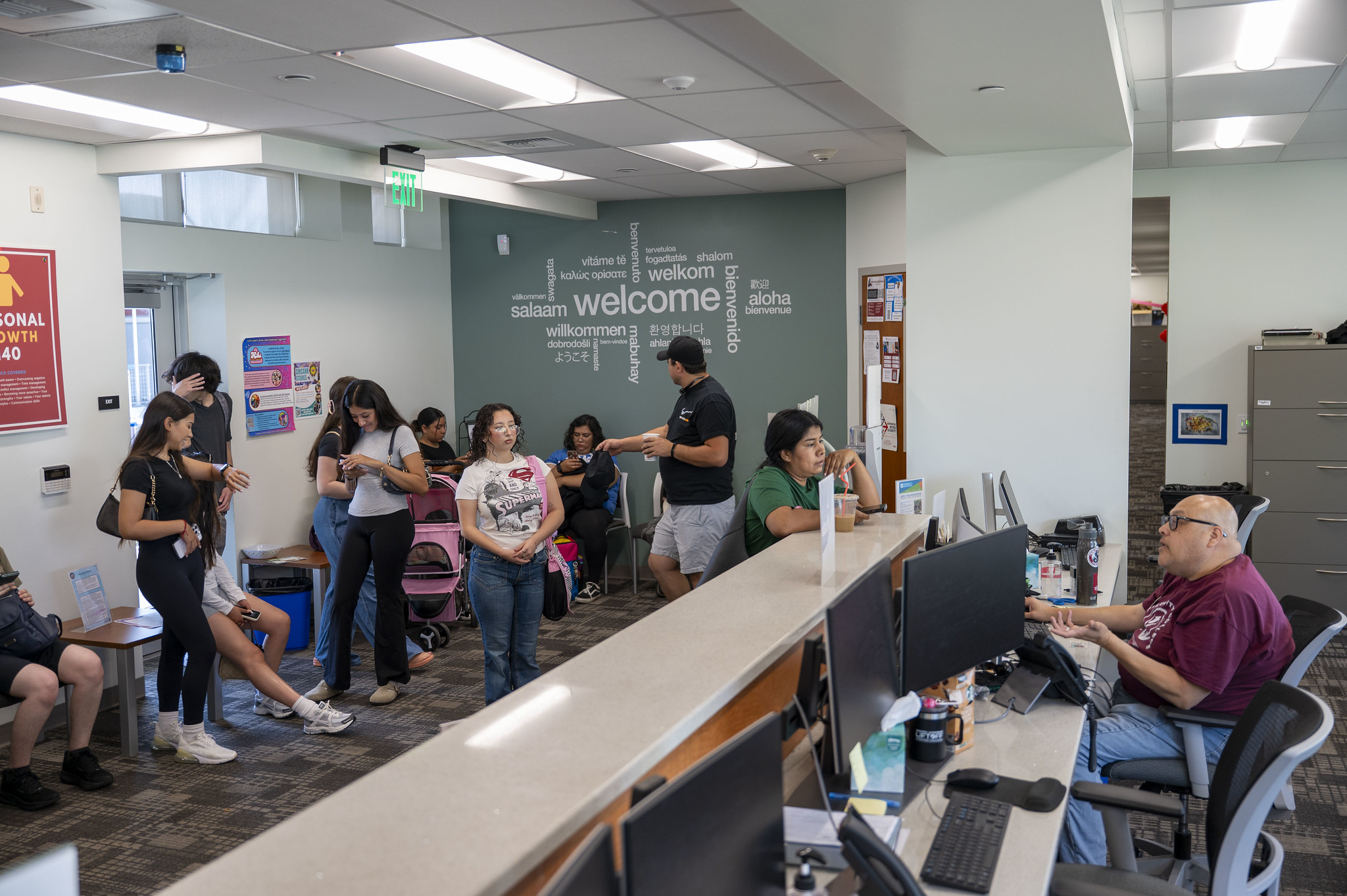 
An employee at a desk helping a student. More students are waiting in line.
