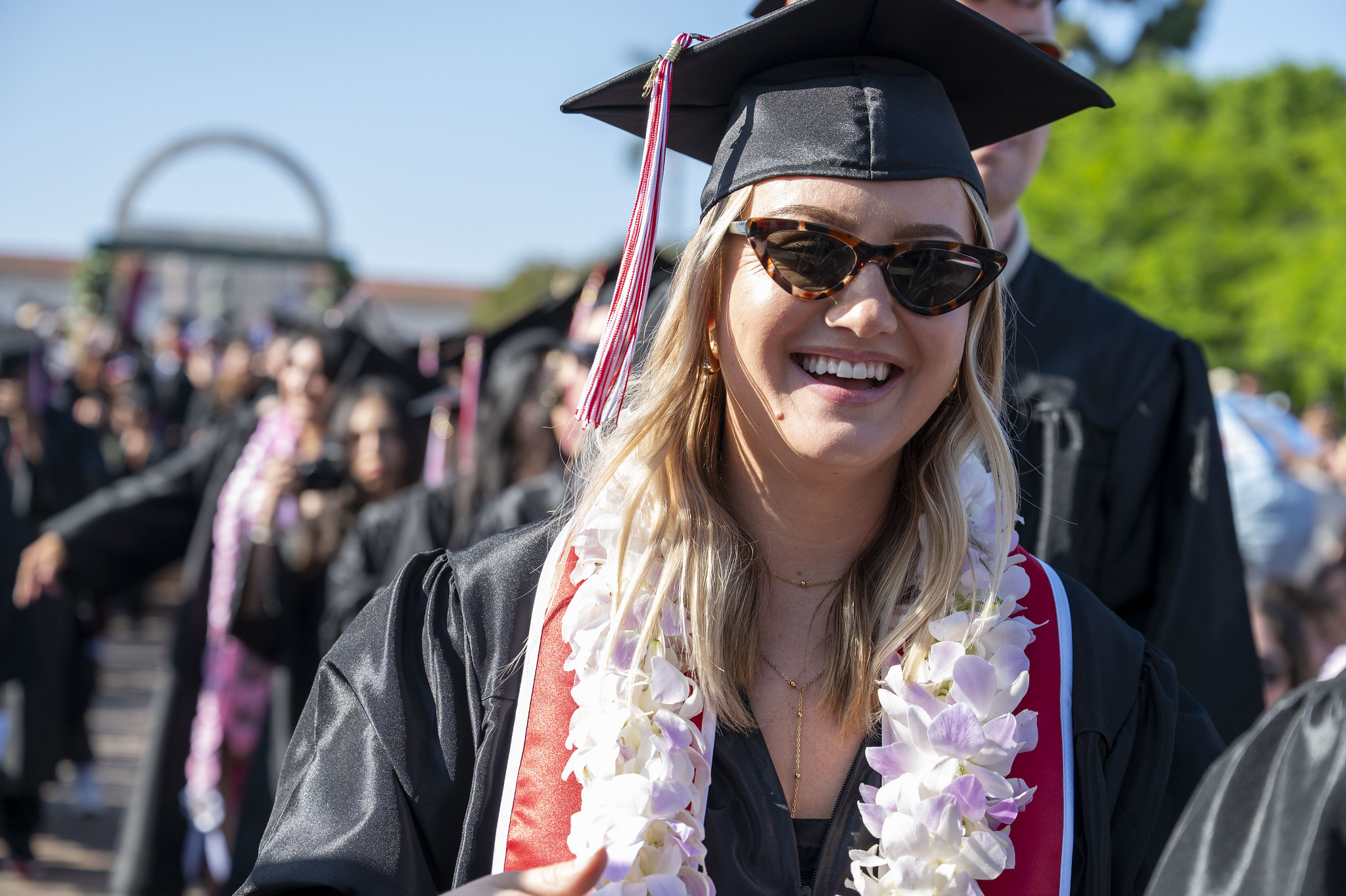 
A graduate wearing a white lei enters commencement to take her seat.
