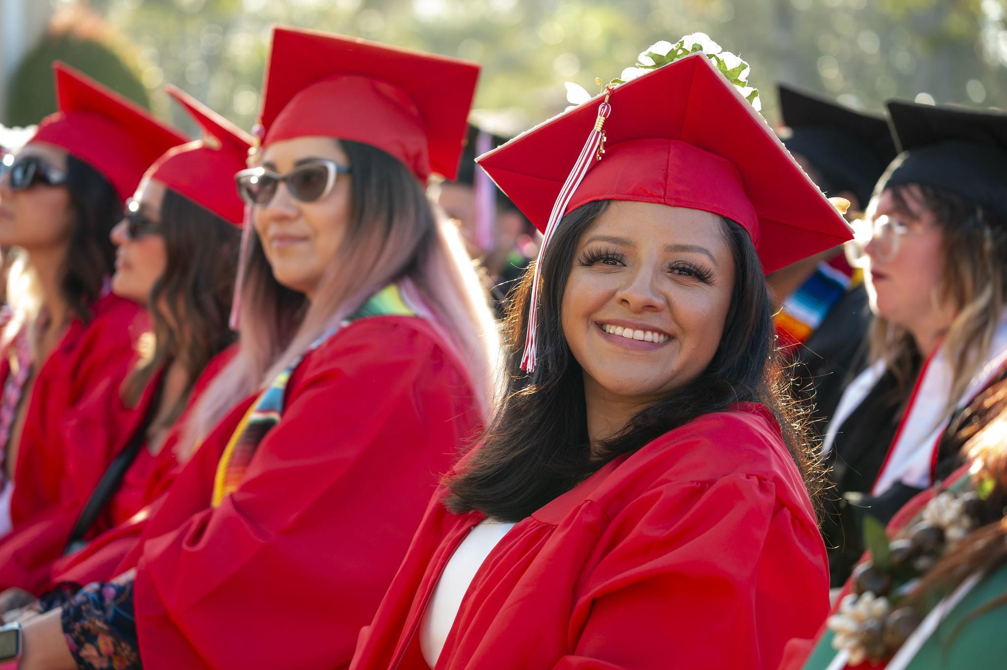 
Four students in red caps and gowns seated during commencement.
