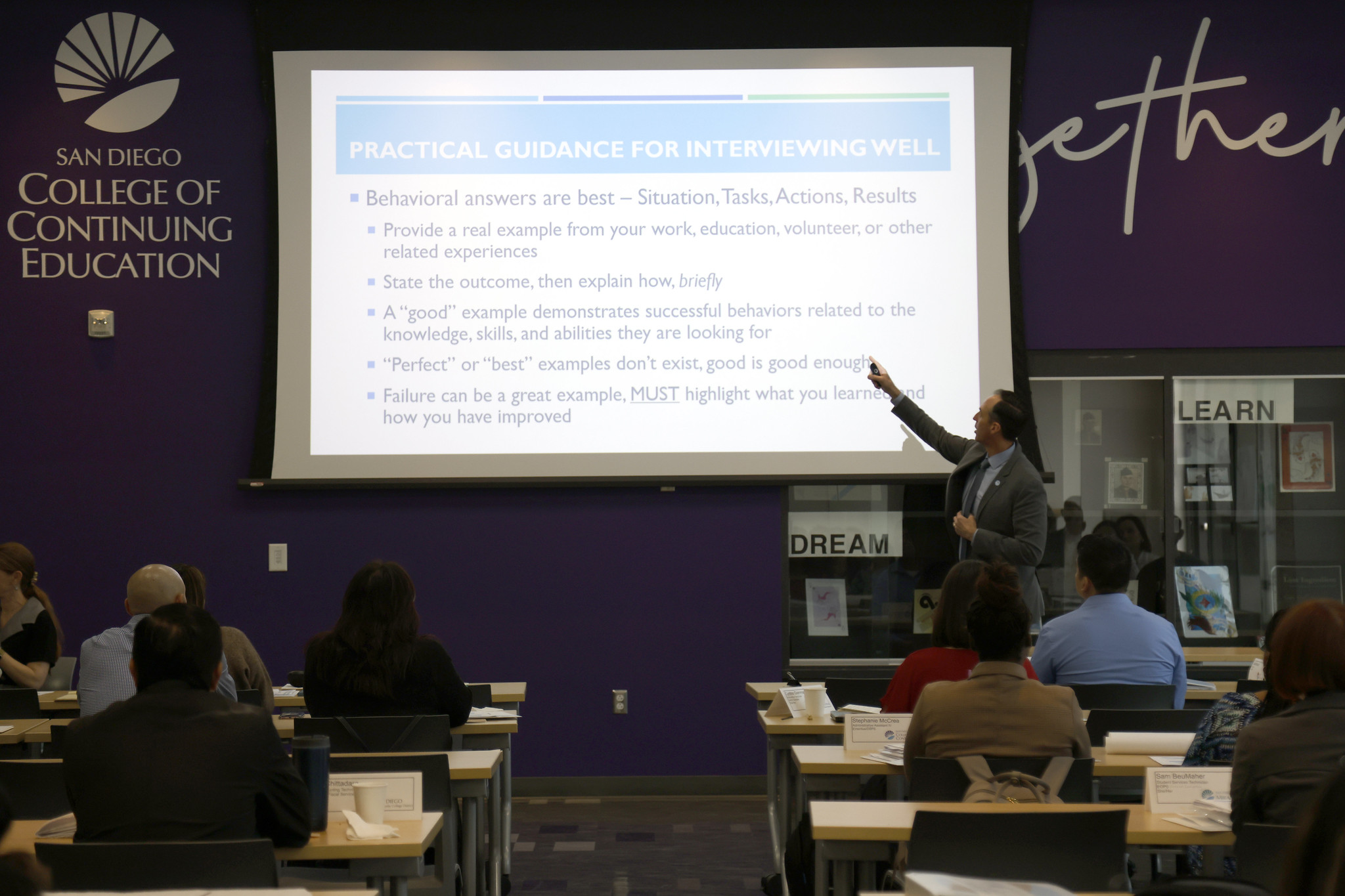 
The chancellor speaking at the event gestures toward the screen.

