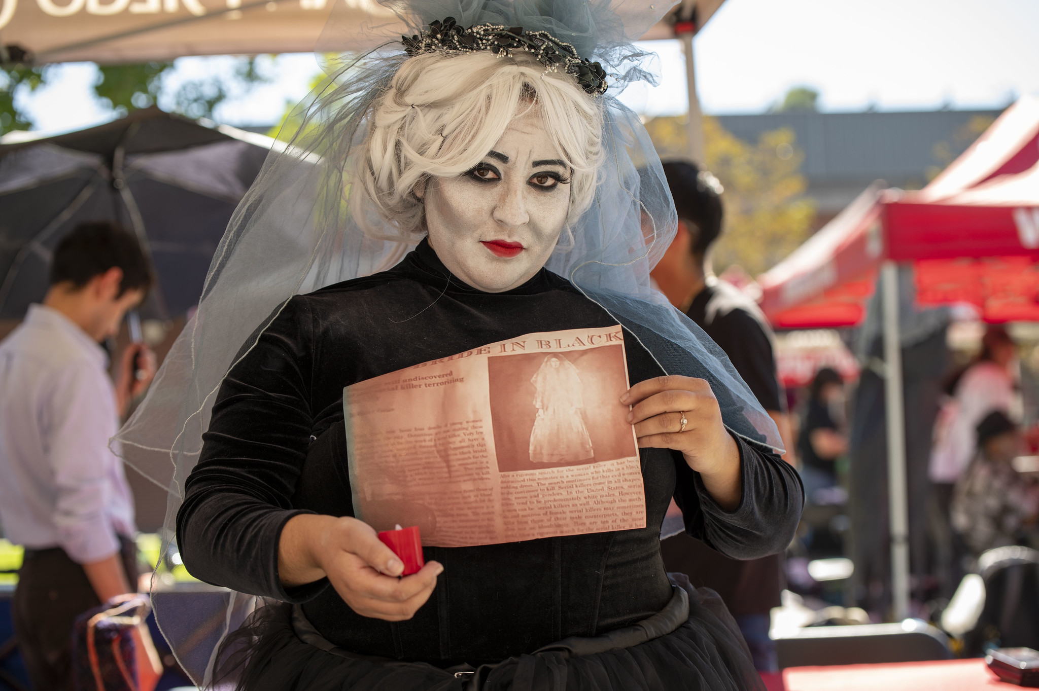 
A woman in a black dress with silver hair and silver face paint is dressed as a ghost.

