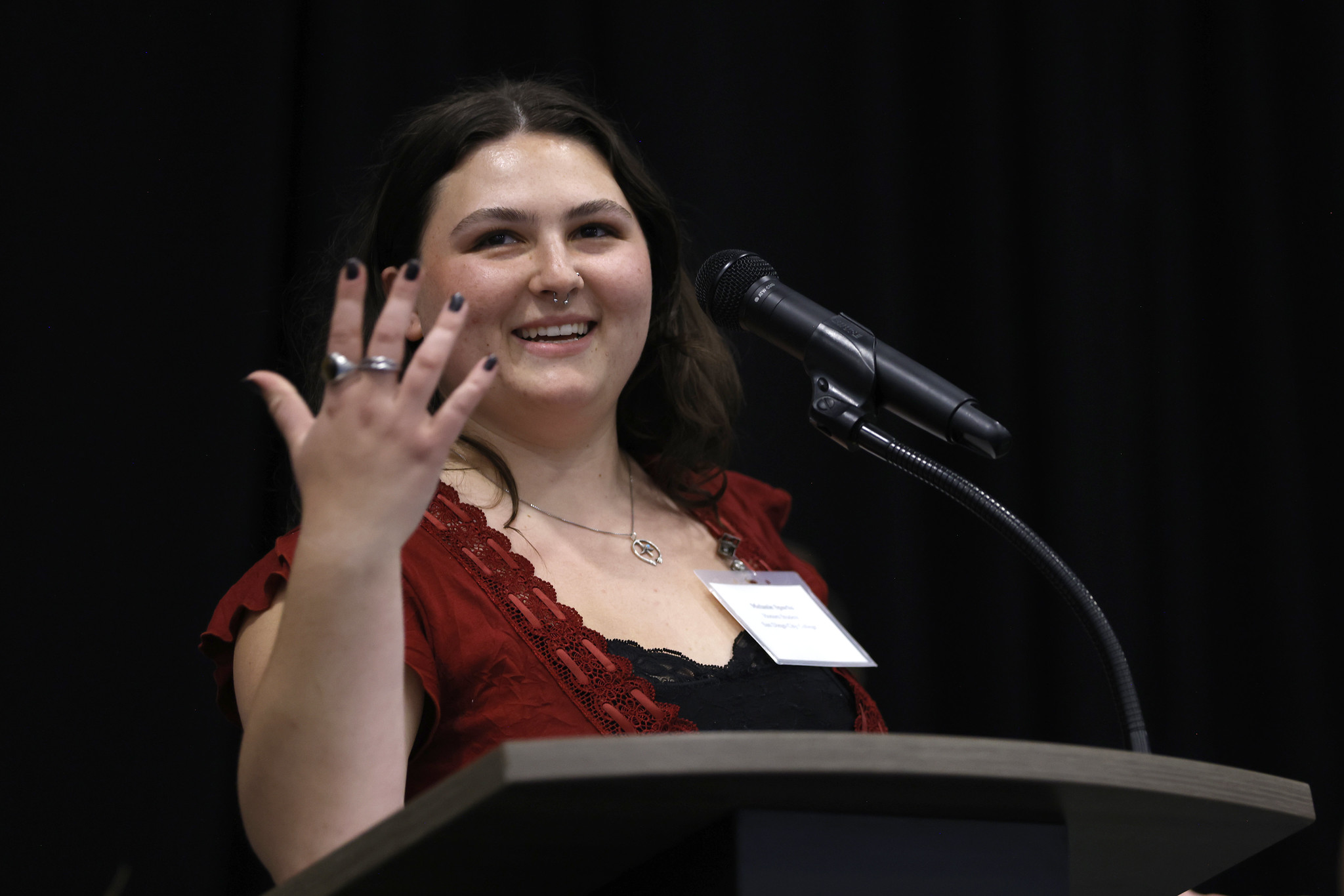 
A student wearing a red shirt gestures while she's speaking at the podium.
