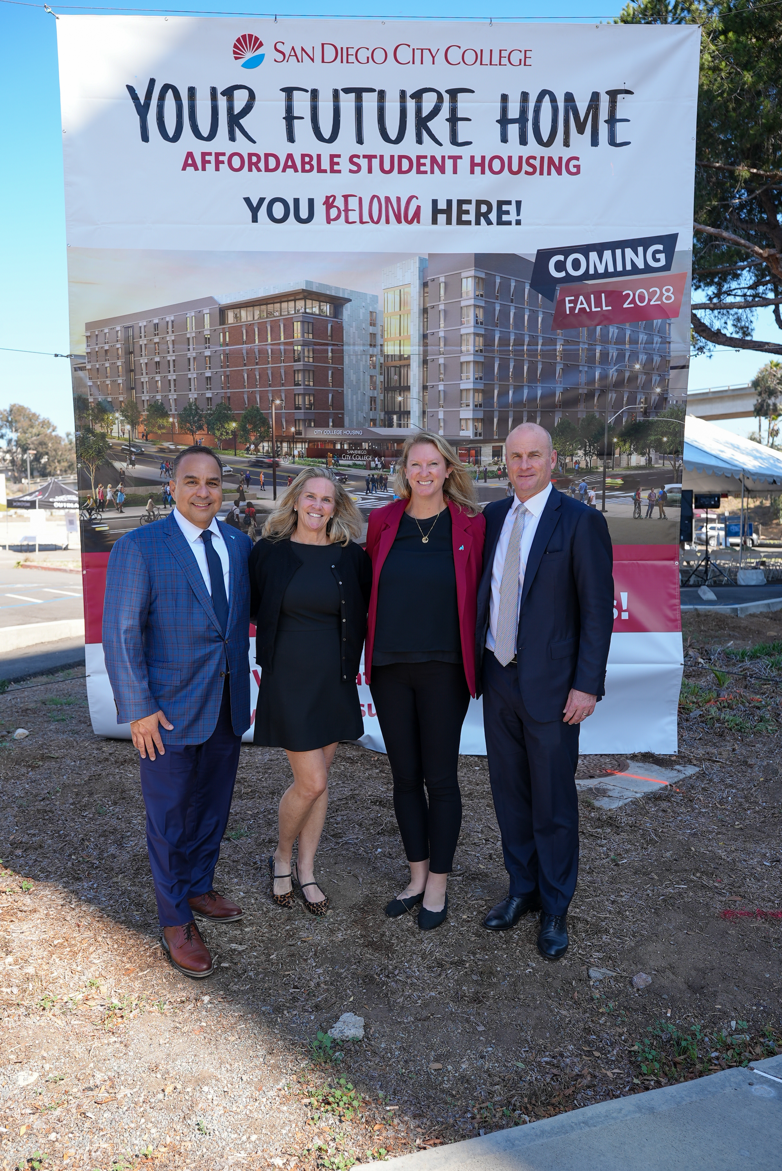 
Four people in front of the banner showing the future student housing project.
