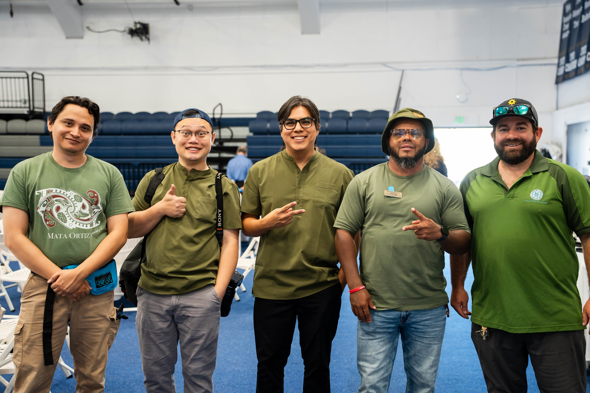 
Five men in green shirts pose for a group photo.
