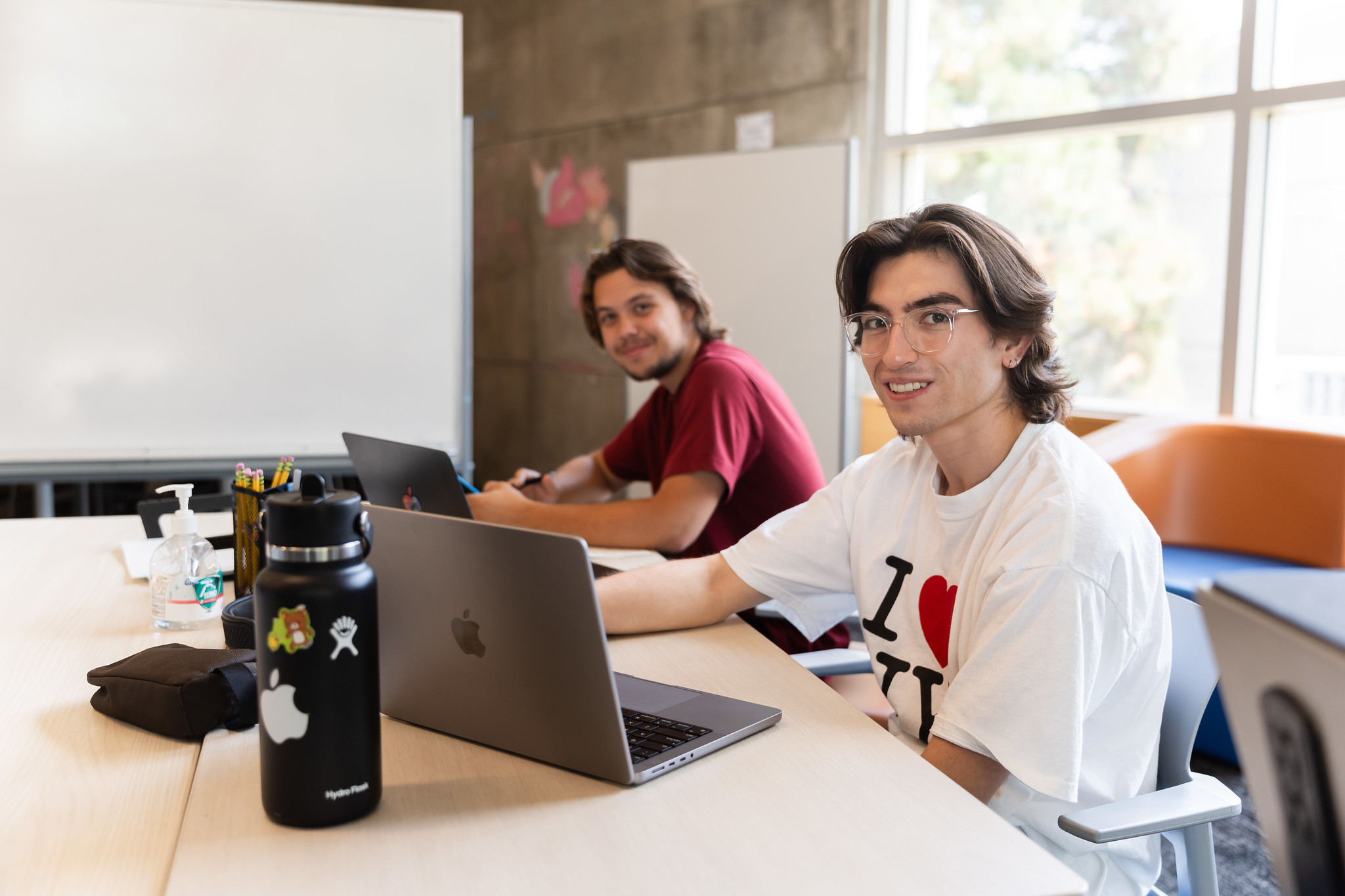 
Two students seated at a table with laptops.
