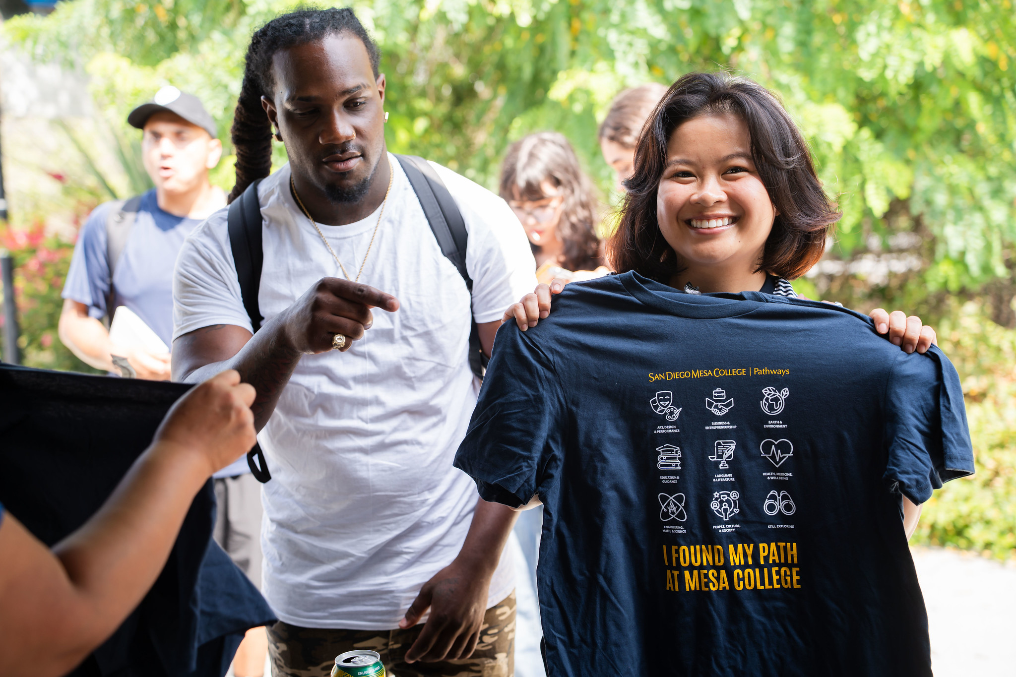 
Two students at a welcome booth. One is holding up a blue Mesa College Pathways t-shirt.
