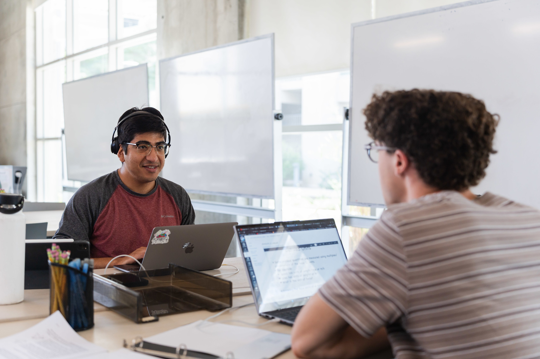 
Two students sitting at a table working on laptops. 
