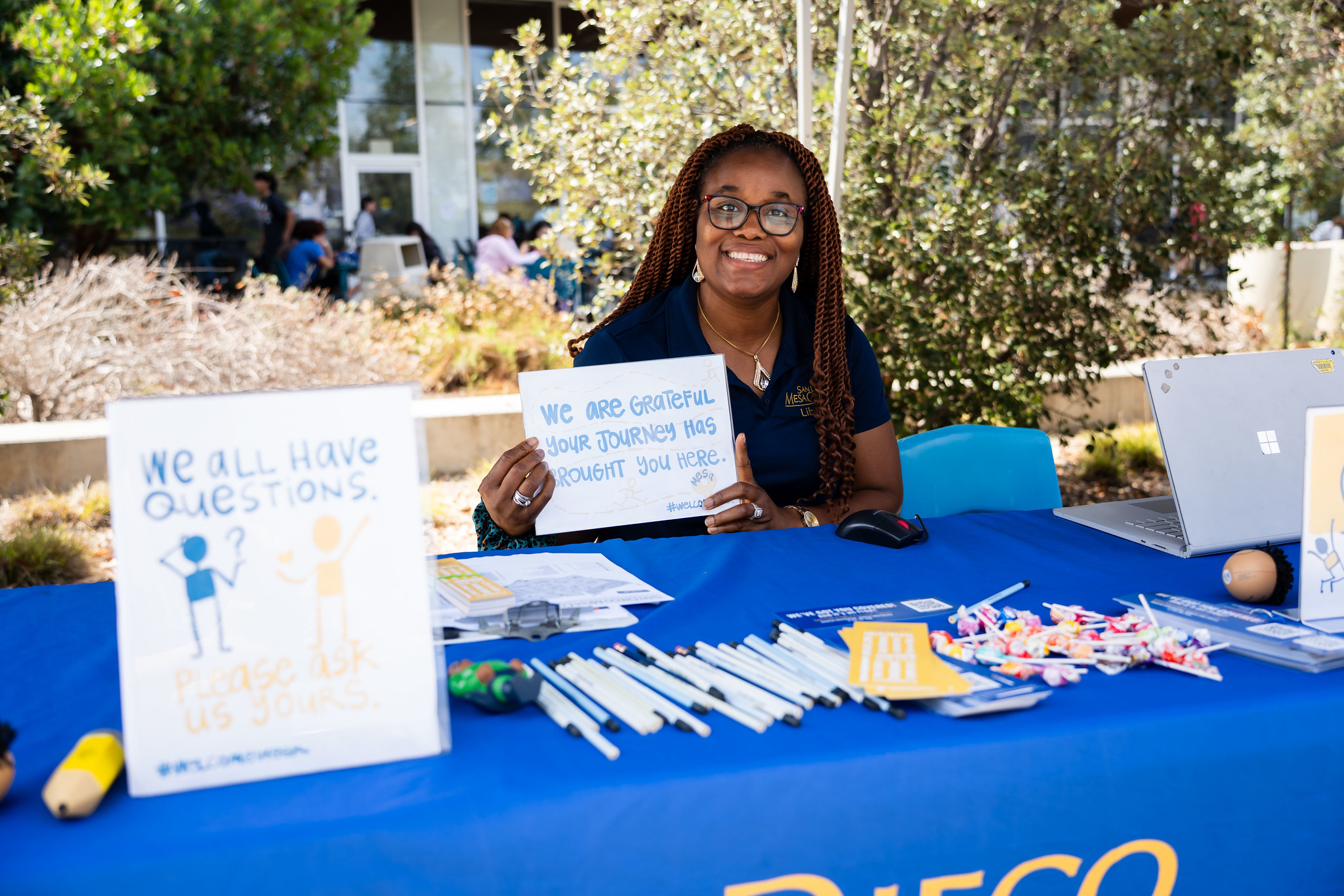 
A woman sits at a table and holds up a small whiteboard that says We are grateful that your journey has brought you here.
