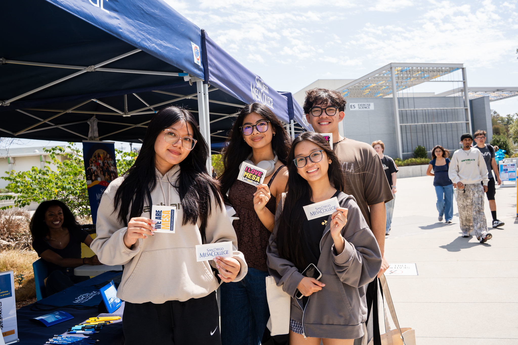 
Four students at a welcome booth hold up Mesa College stickers.

