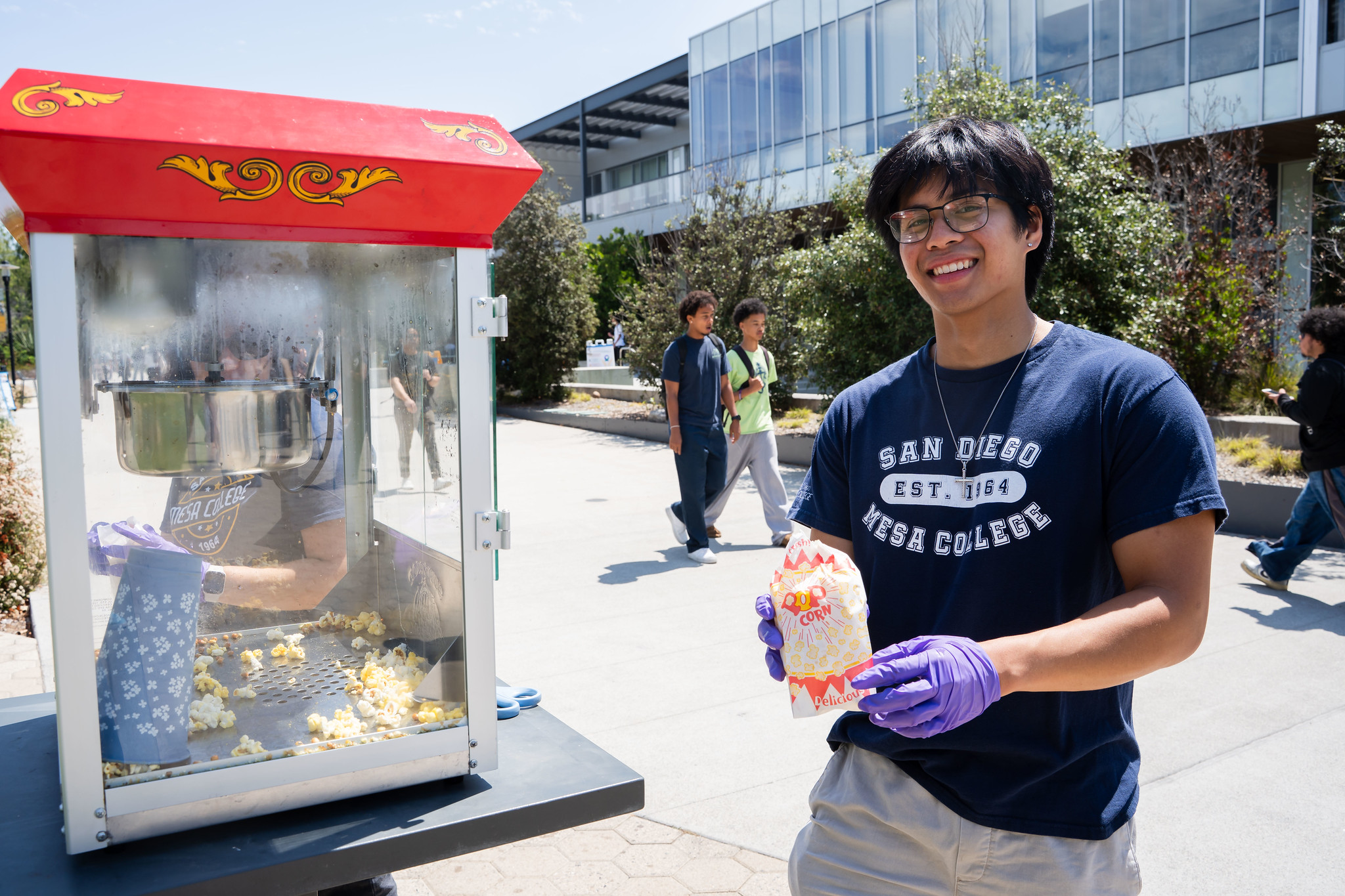 
A man in a blue Mesa College t-shirt on campus serving small bags of popcorn.
