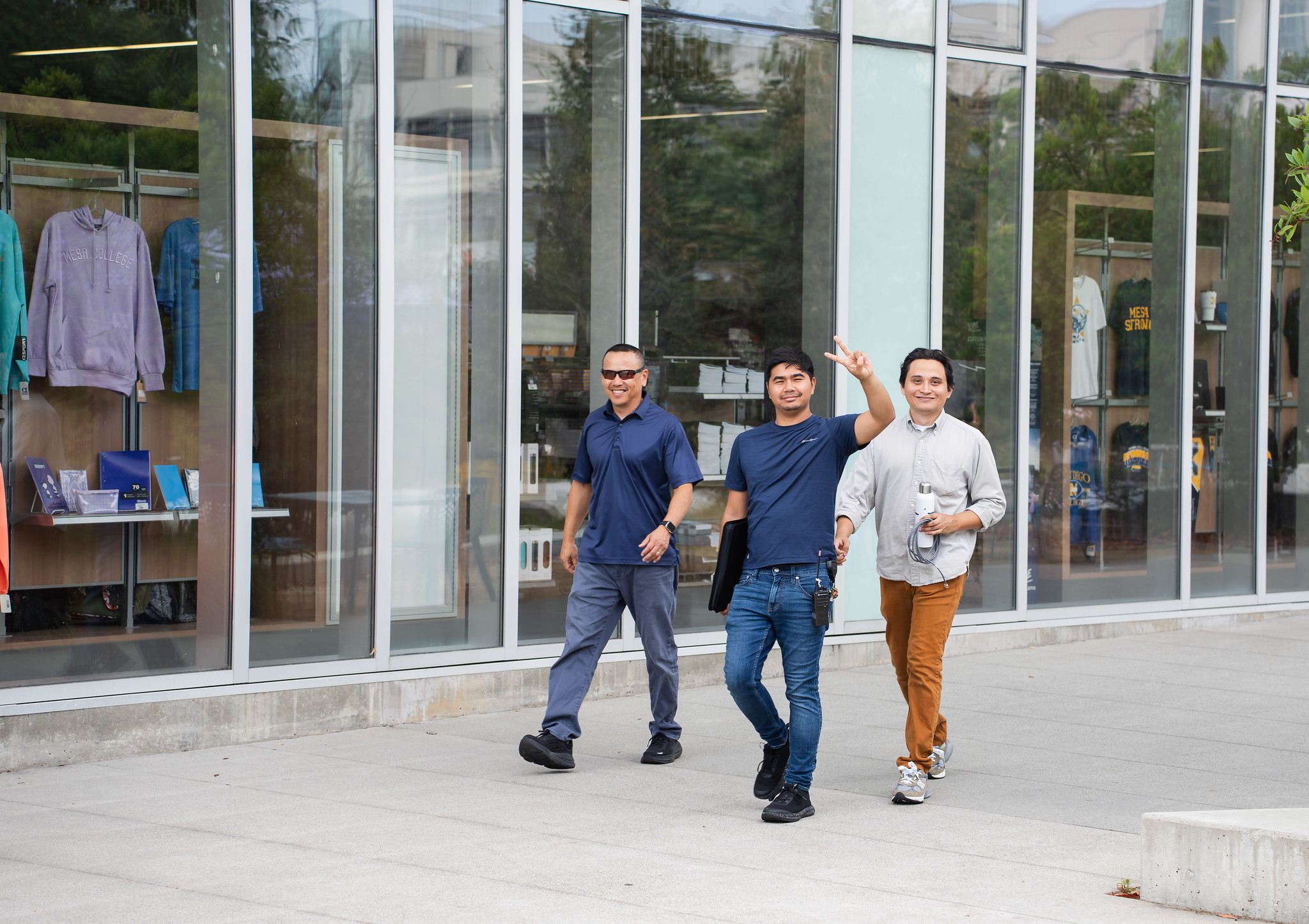 
Three students walking on campus wave to the camera.
