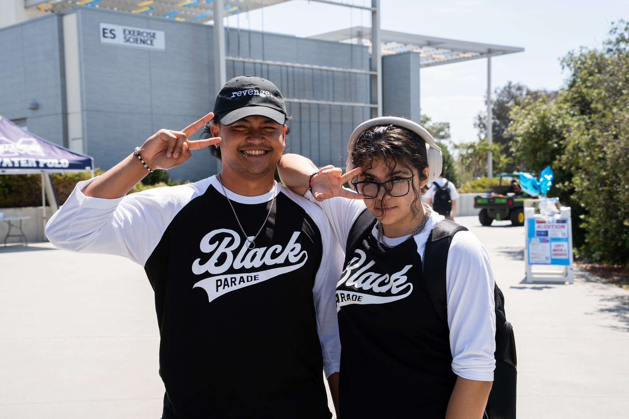 
Two people in matching black and white jerseys that say Black Parade give a peace sign.
