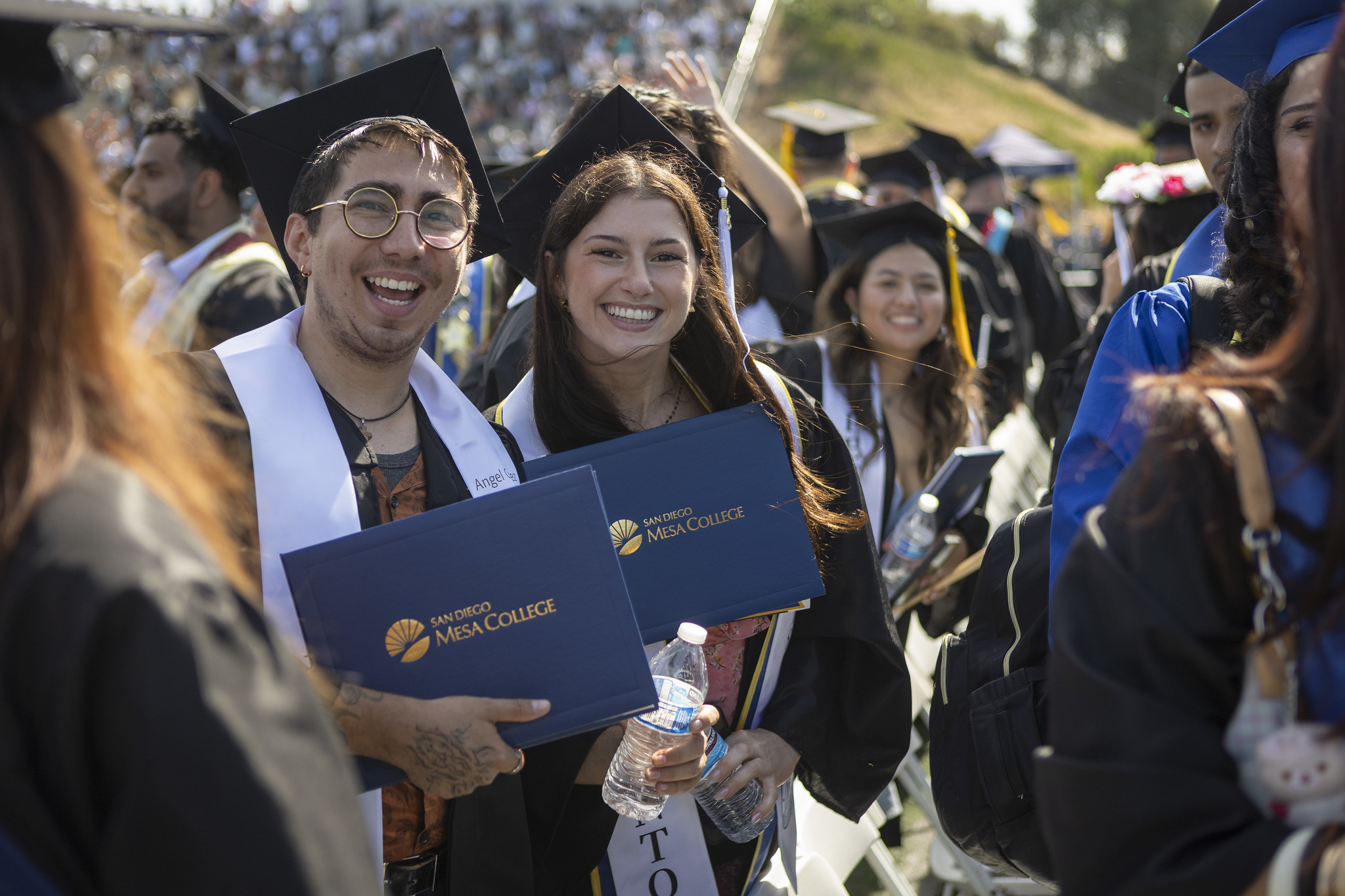 
Two students in the audience hold up their degrees.
