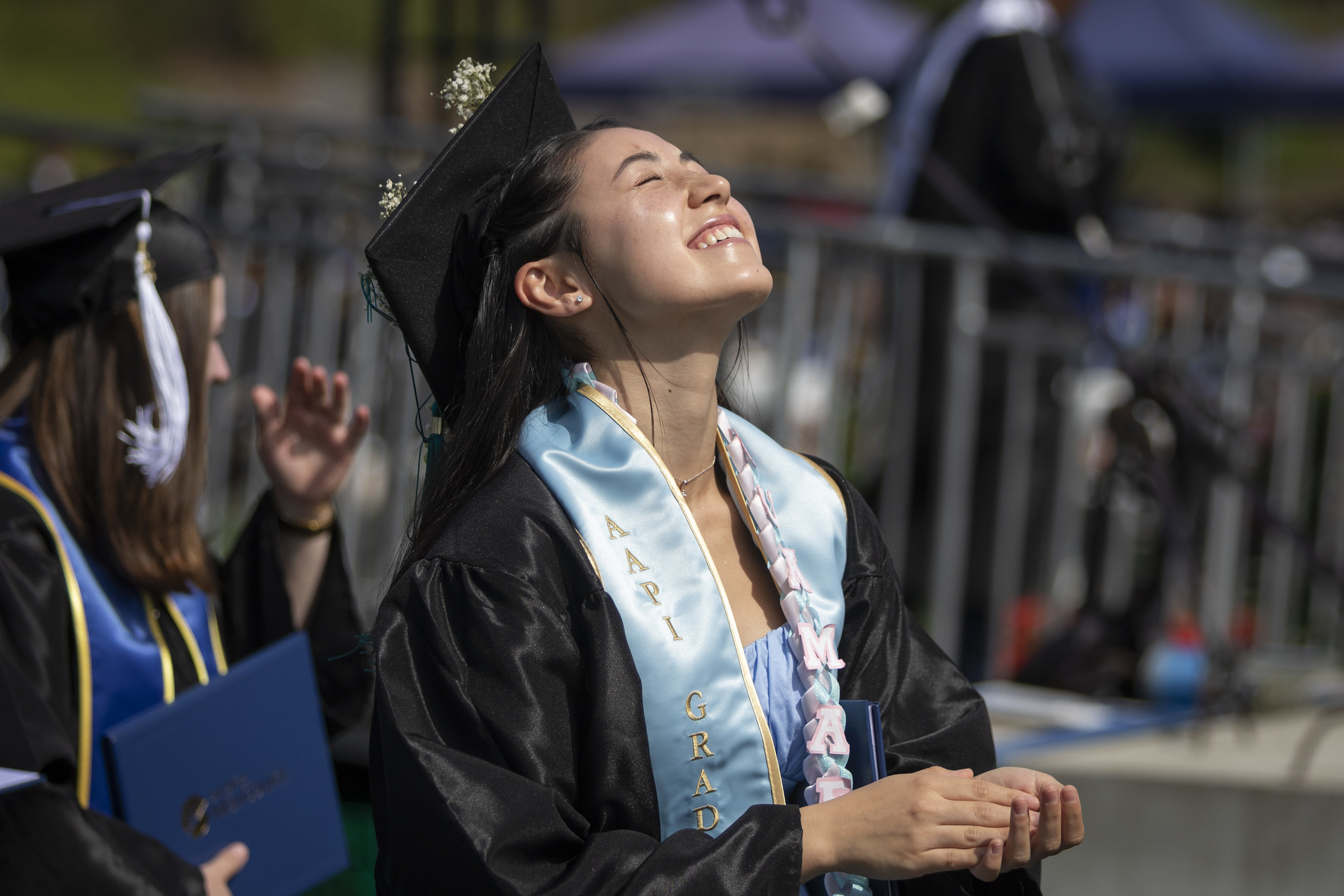 
A graduate closes her eyes and lifts her face toward the sun while seated at commencement.

