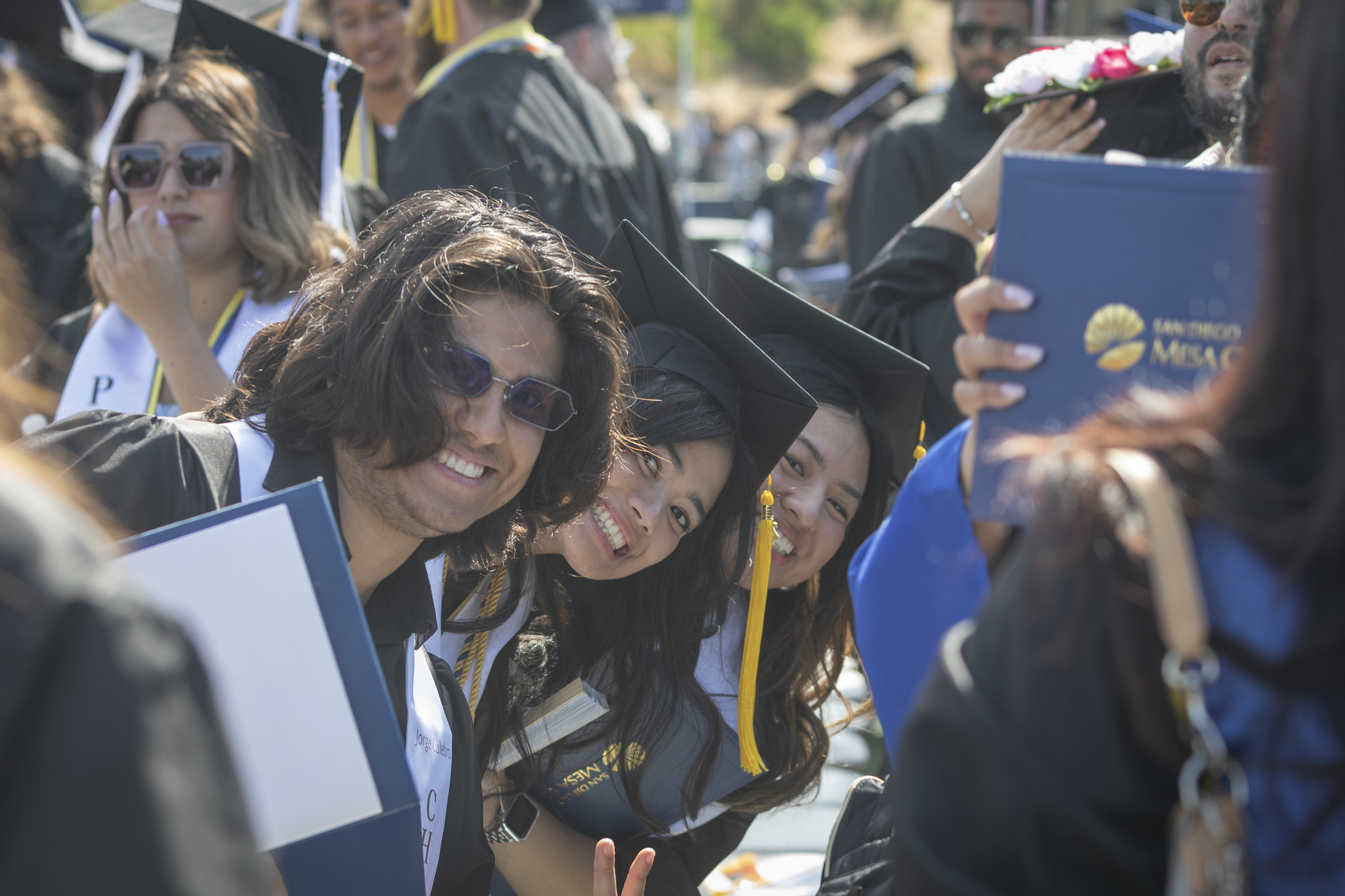 
Three students seated in the audience hold up their degrees.
