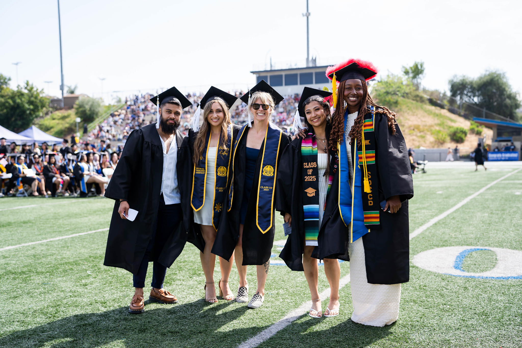 
Five graduates line up for a group photo on the field at commencement.
