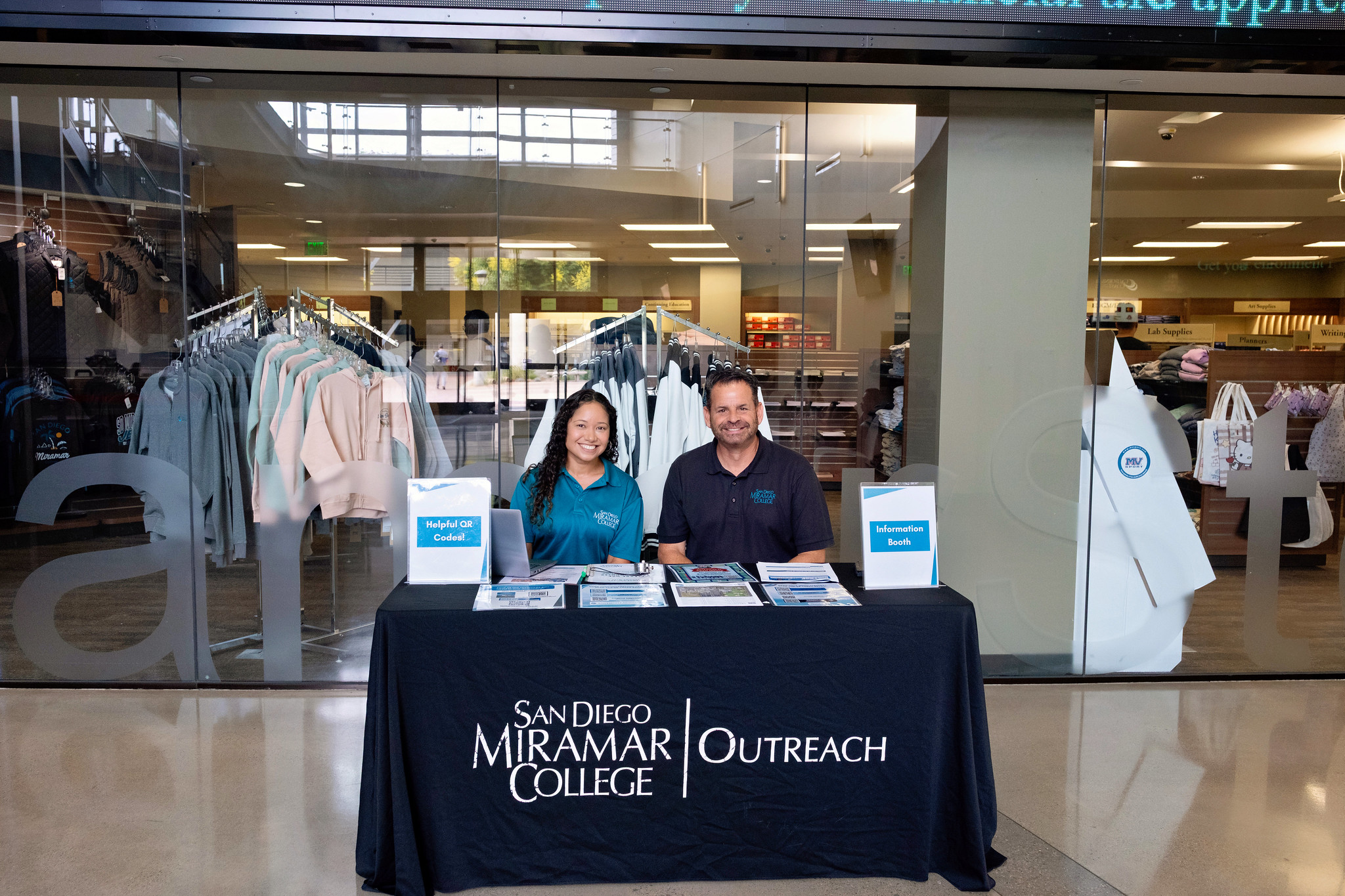 
Two employees at the table for student outreach, outside the Miramar bookstore.
