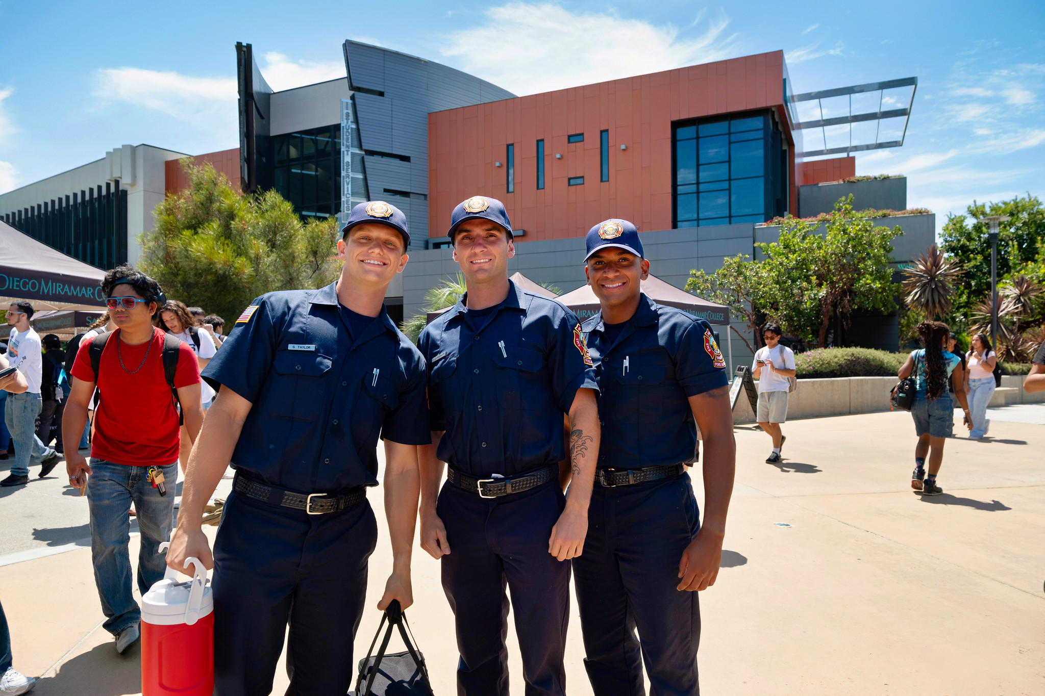 
Three cadets wear blue fire academy uniforms and baseball caps.
