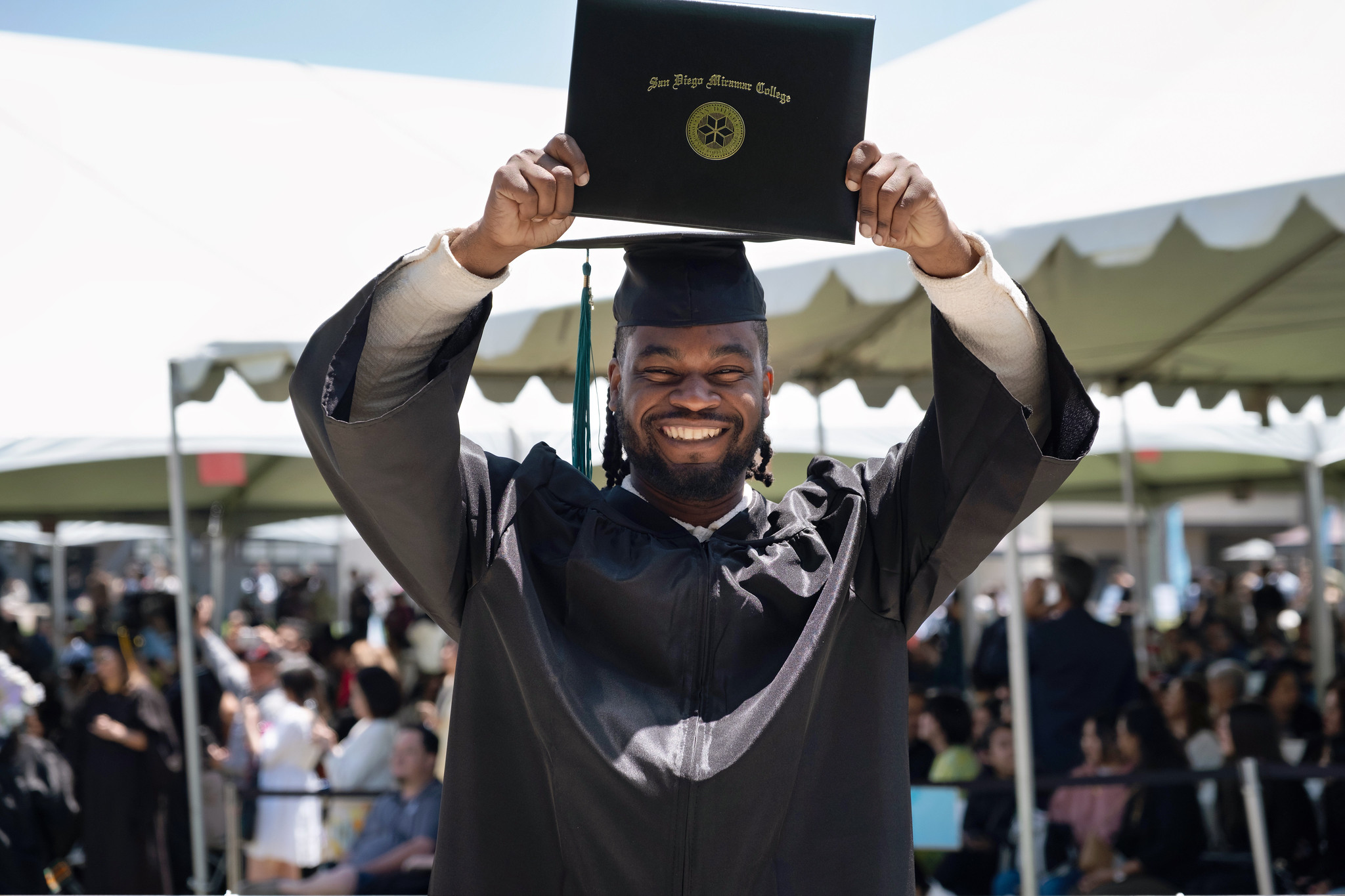 
A graduate is smiling and holding his degree over his head.

