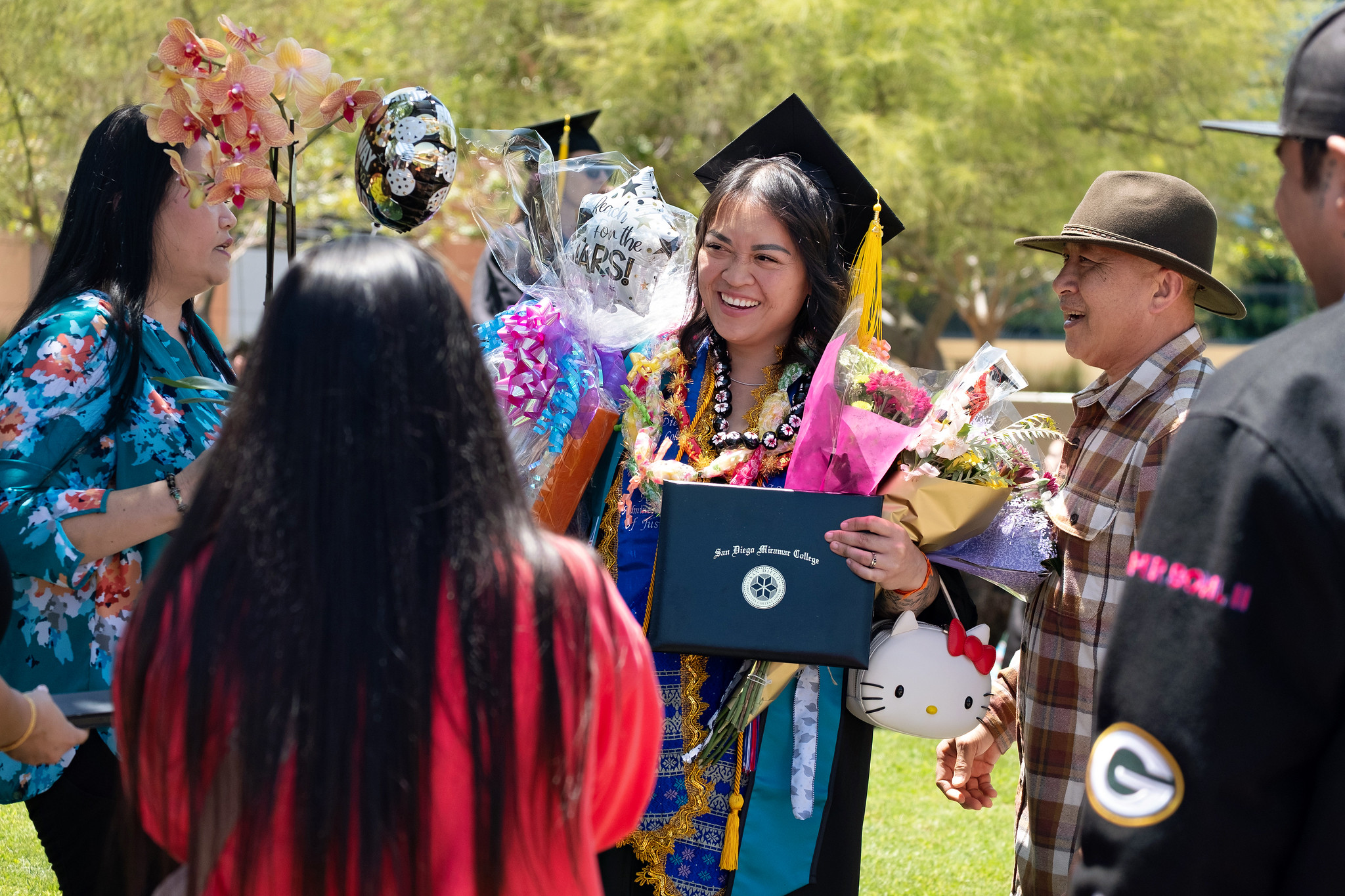 
A graduate with her degree and holding flowers celebrates with her family.
