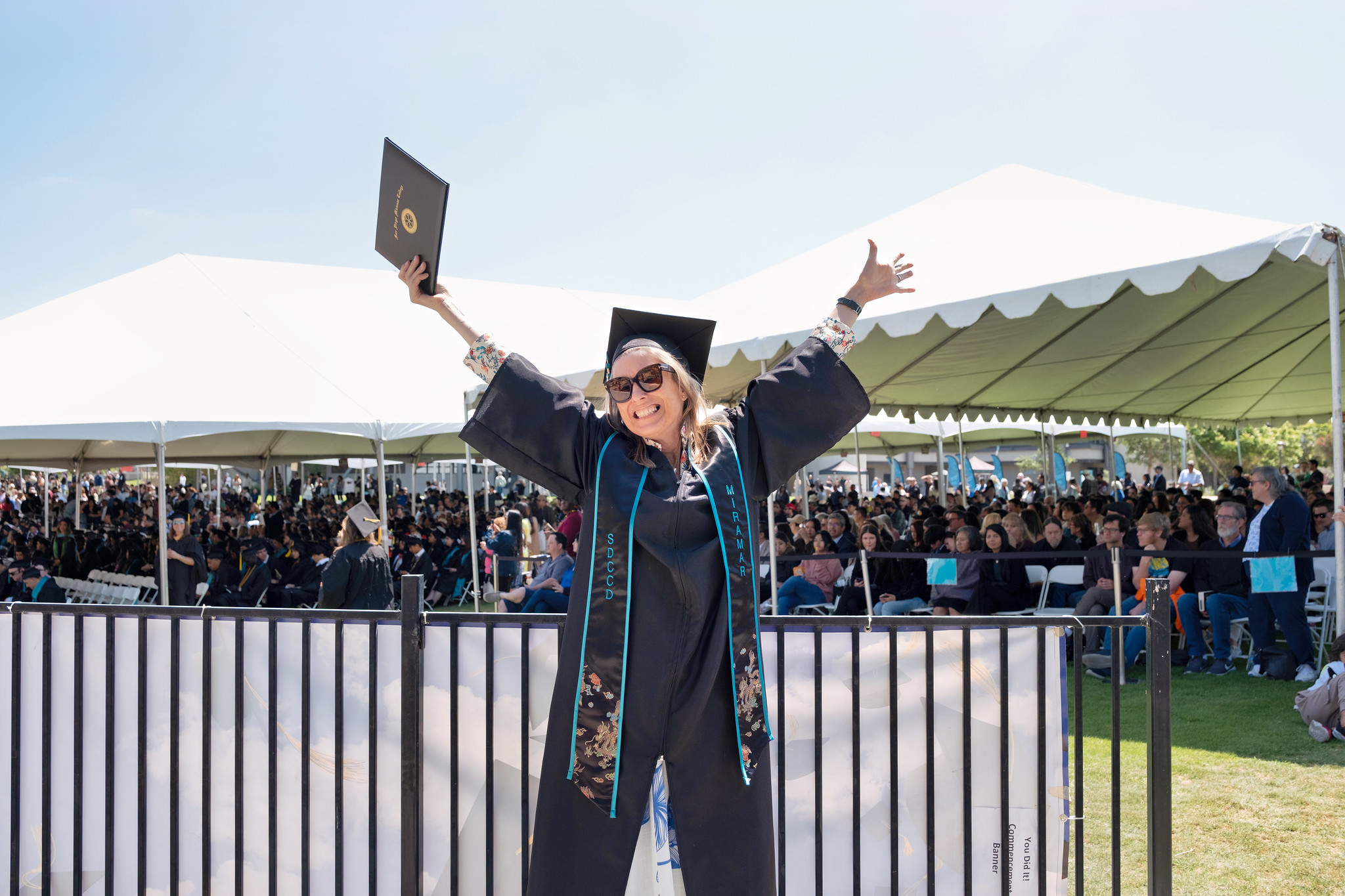 
A graduate celebrating with both hands over her head with her degree.

