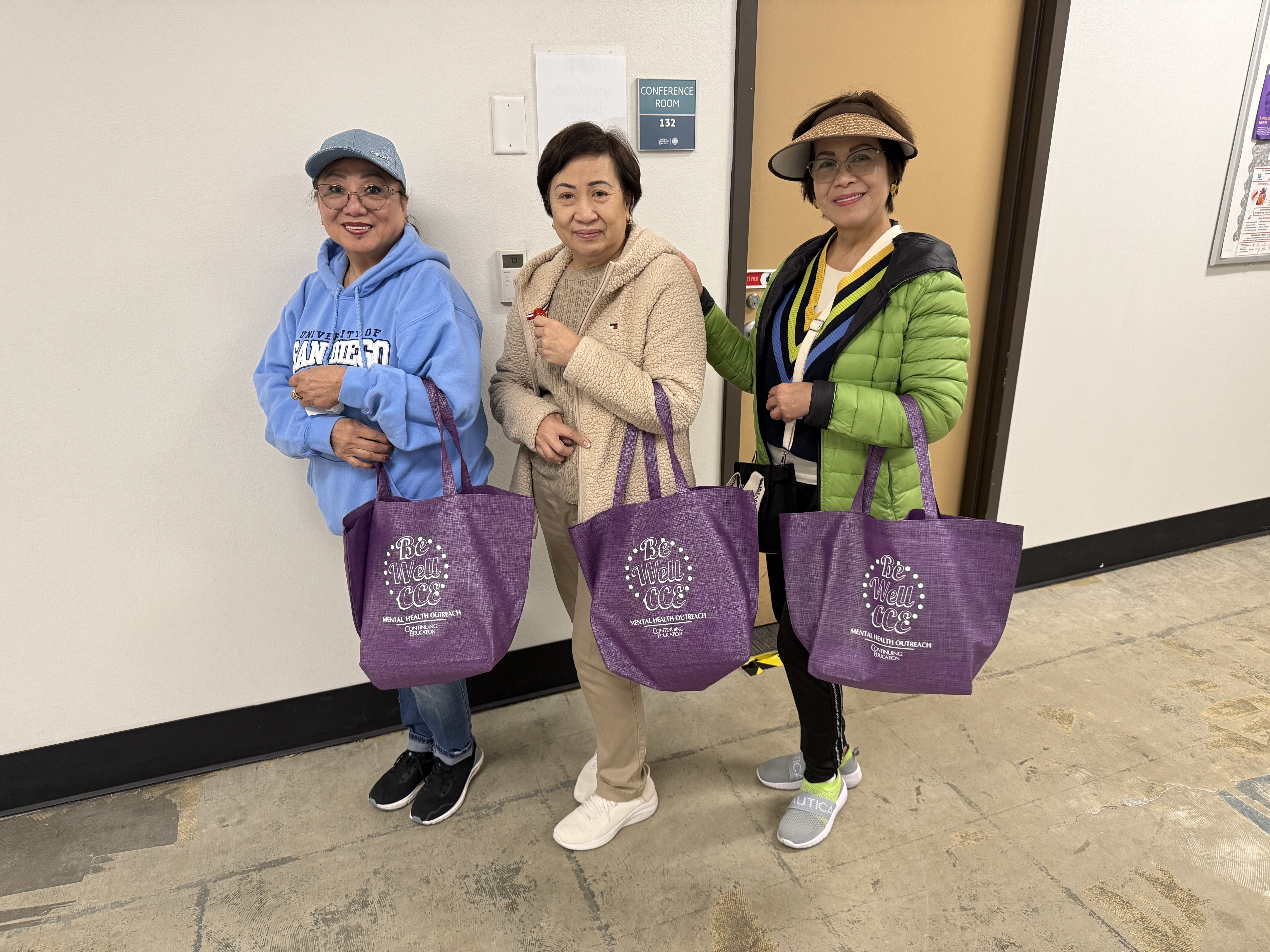 
Three ladies hold up purple tote bags that they received during welcome week at College of Continuing Education.
