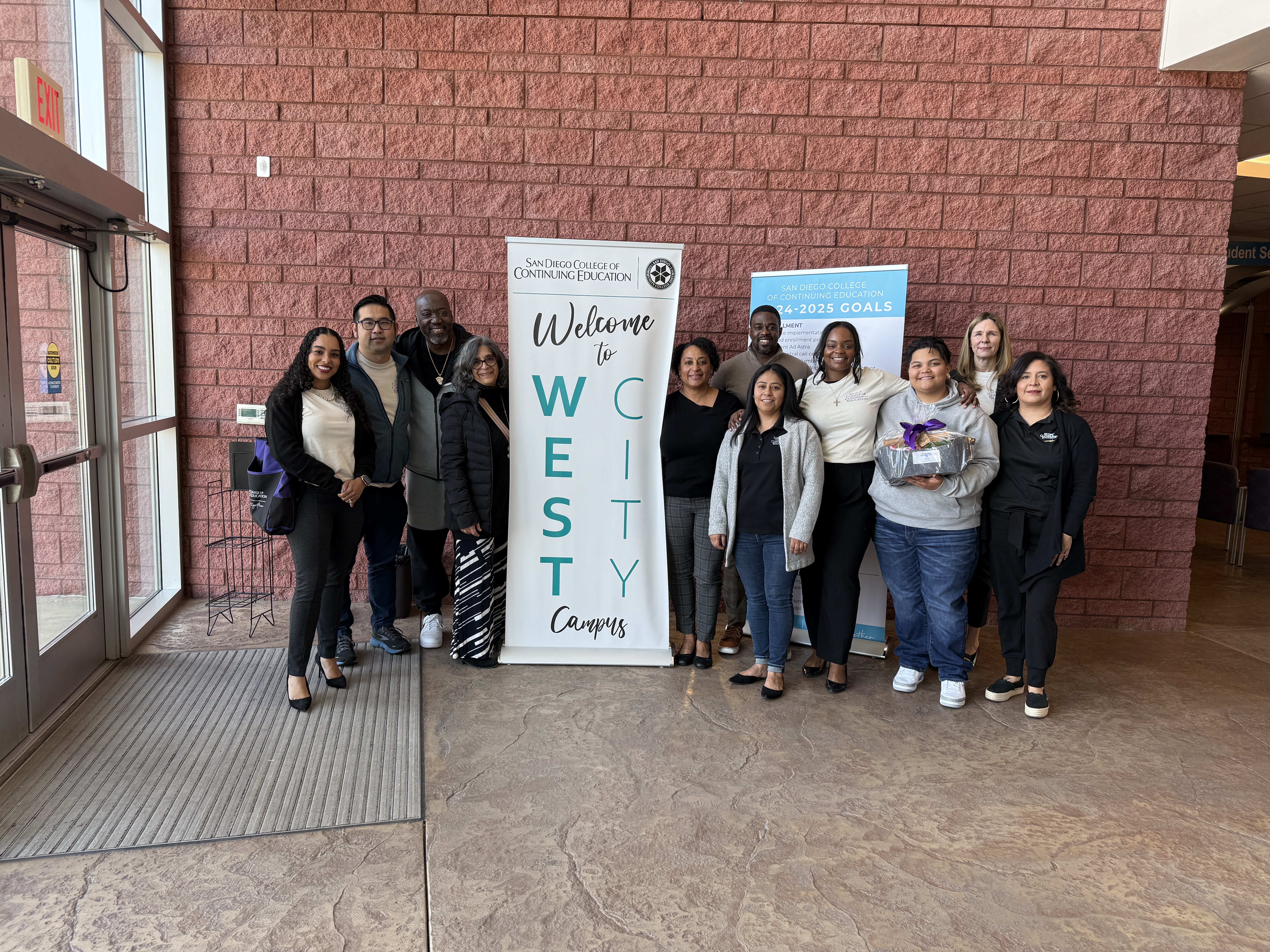 
Eleven people stand around a welcome banner at the West City campus.
