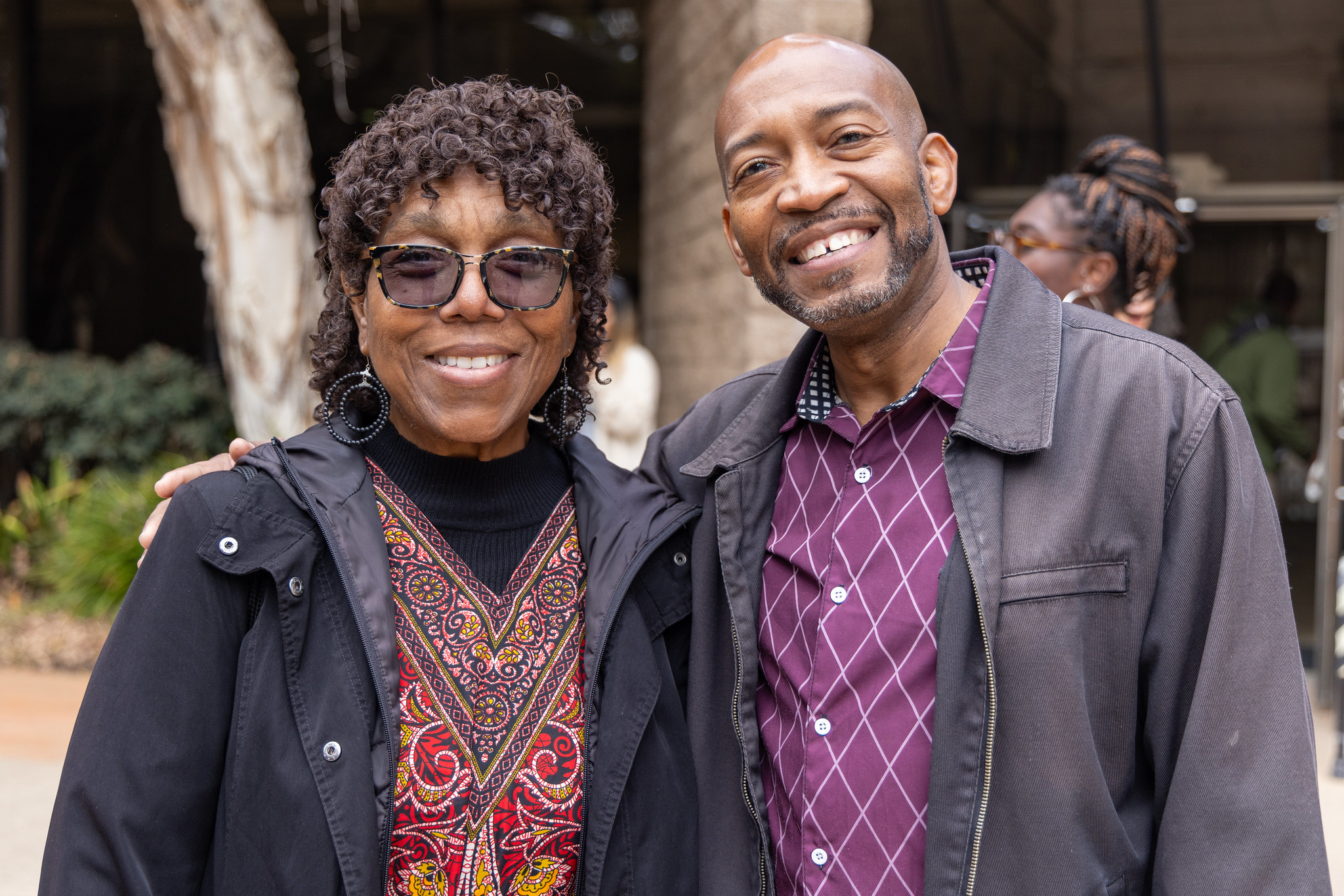 
Two people outside by some trees at the Educational Cultural Complex.
