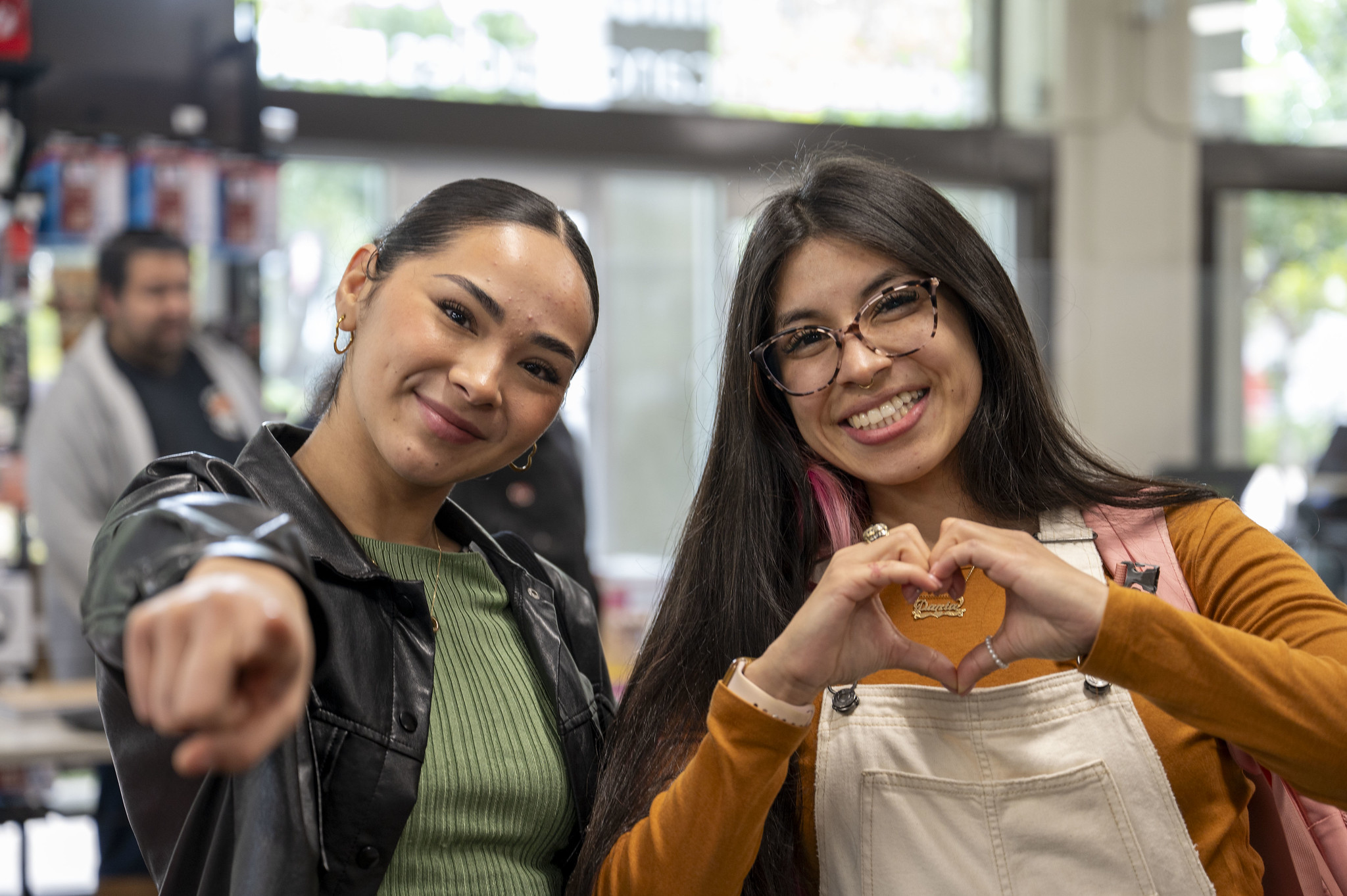 
Two students in the City College bookstore. One lady is pointing to the camera and the other is making a heart with her hands.
