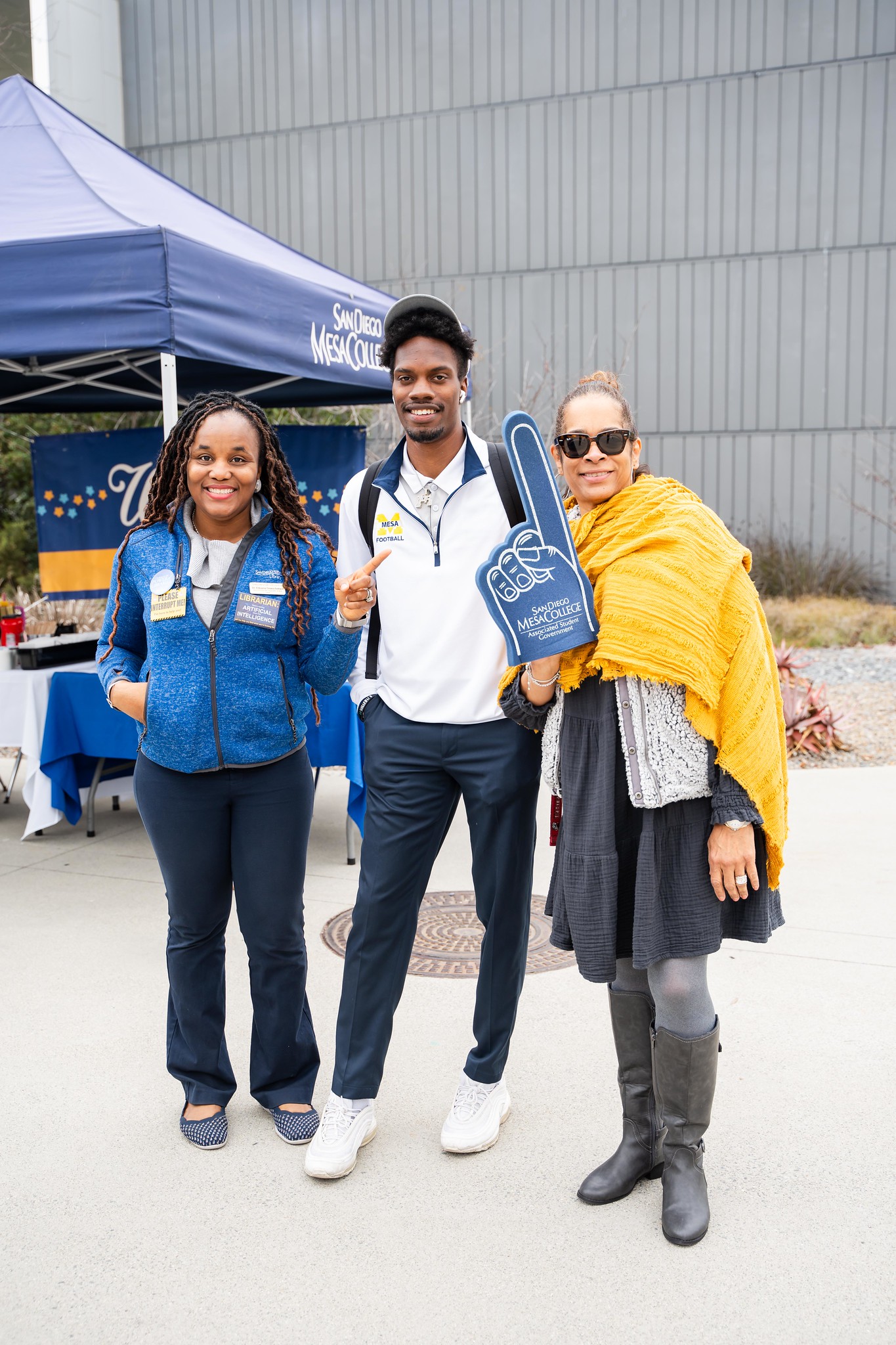 
Three workers at a welcome week booth at Mesa College. One is holding up a giant foam finger.
