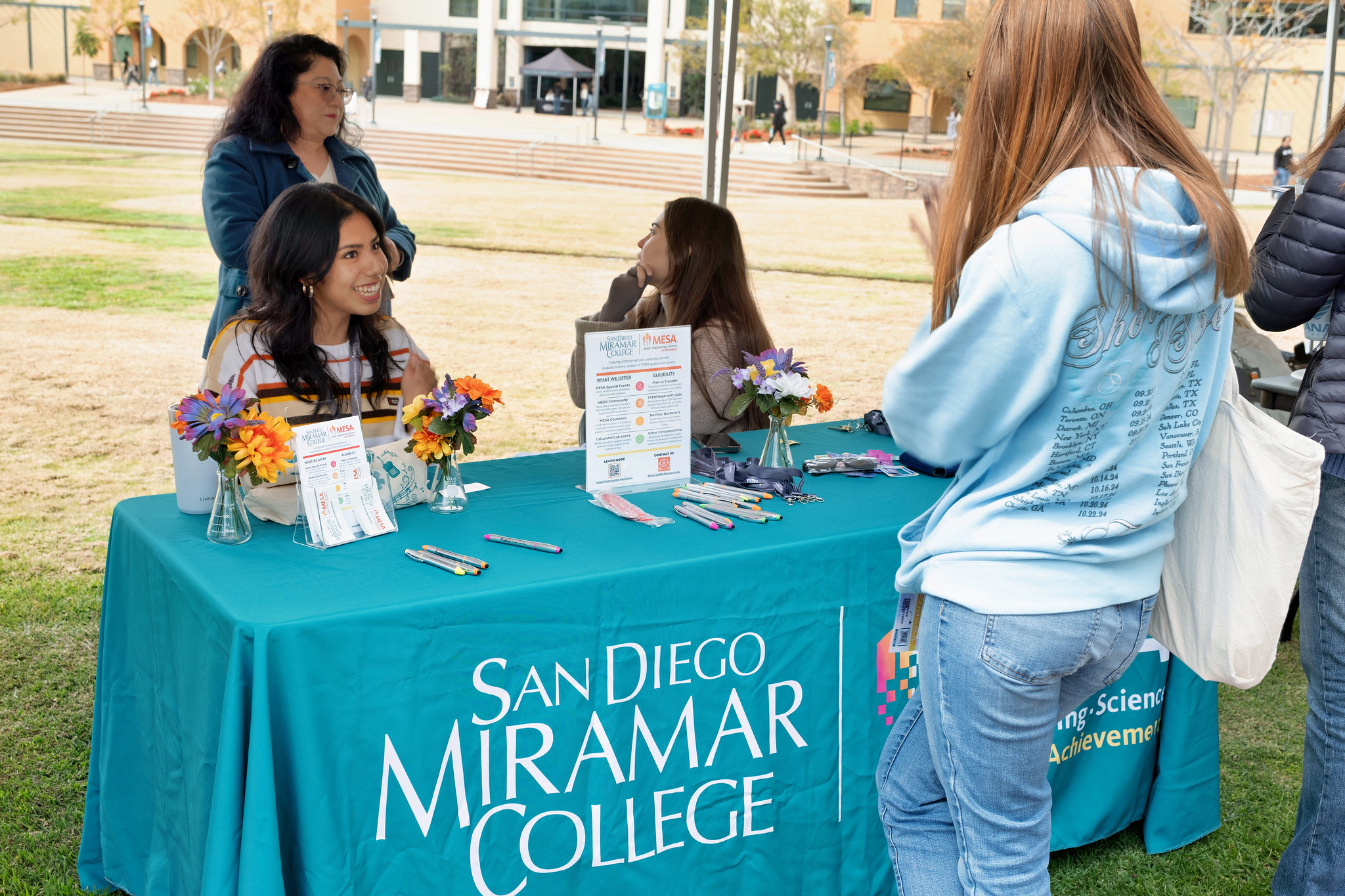 
Three people working at a welcome week booth at Miramar College greet a student.
