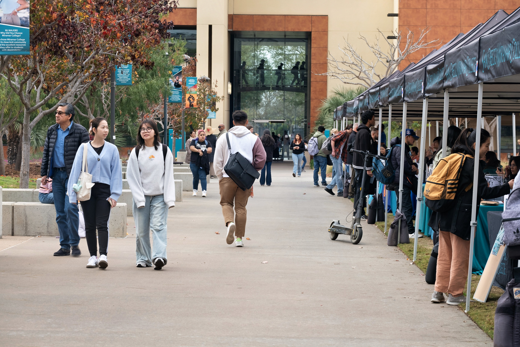 
Students walking past welcome booths at Miramar College toward a building of classrooms.
