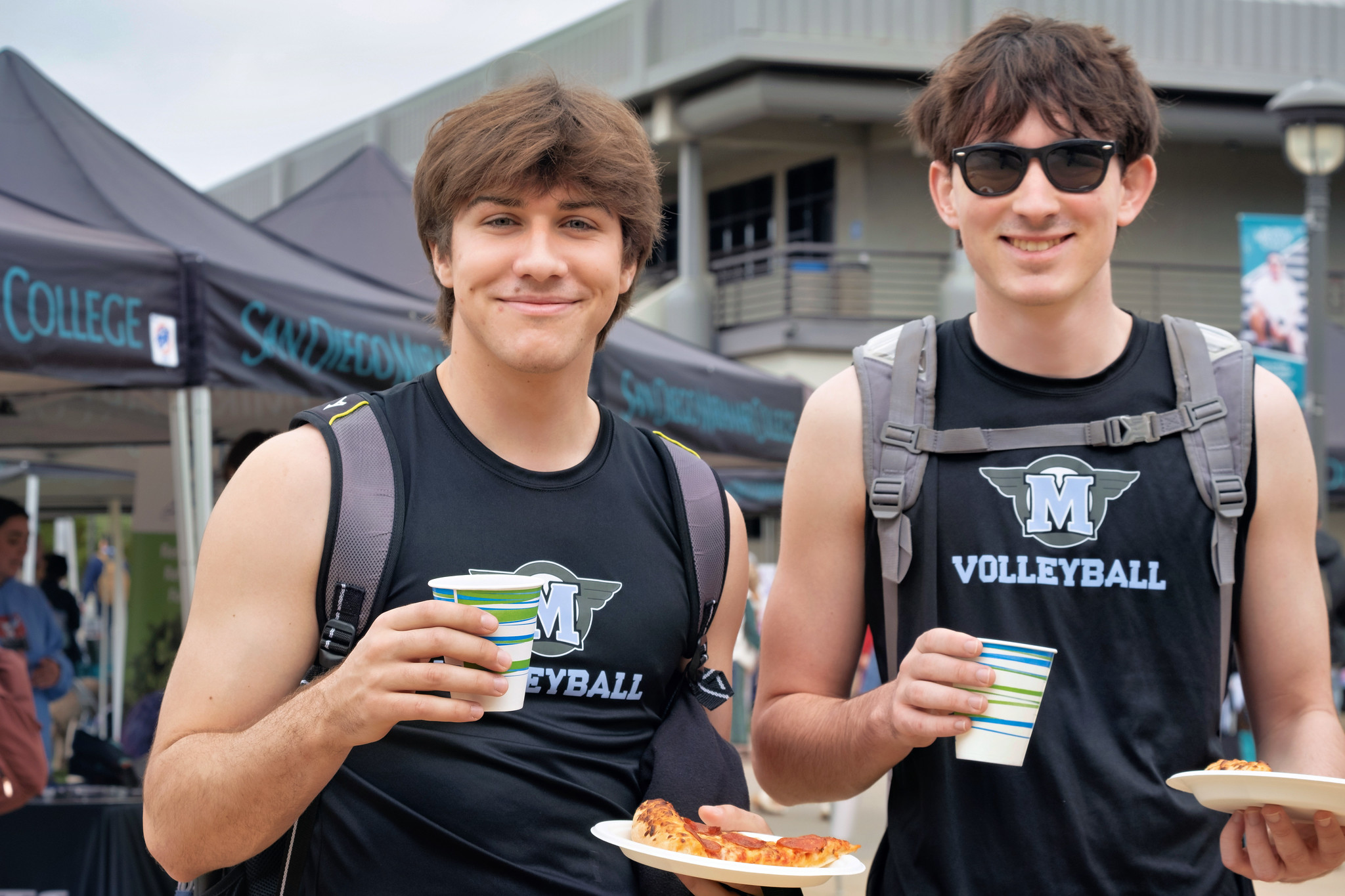 
Two students wearing Miramar men's volleyball tanks hold up their pizza and drinks that they received at welcome week.
