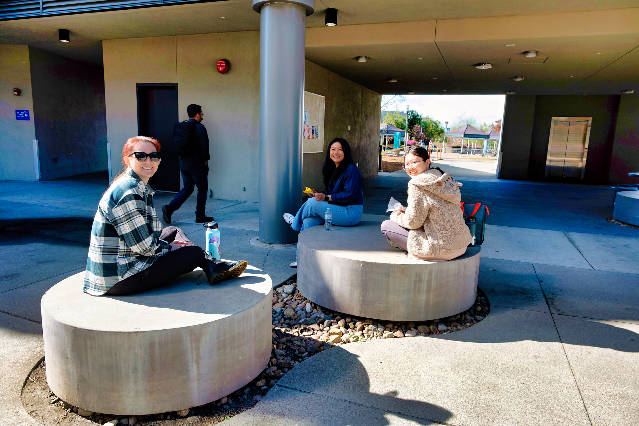 
Three students sit on round cement seats outside of a building at Miramar College.
