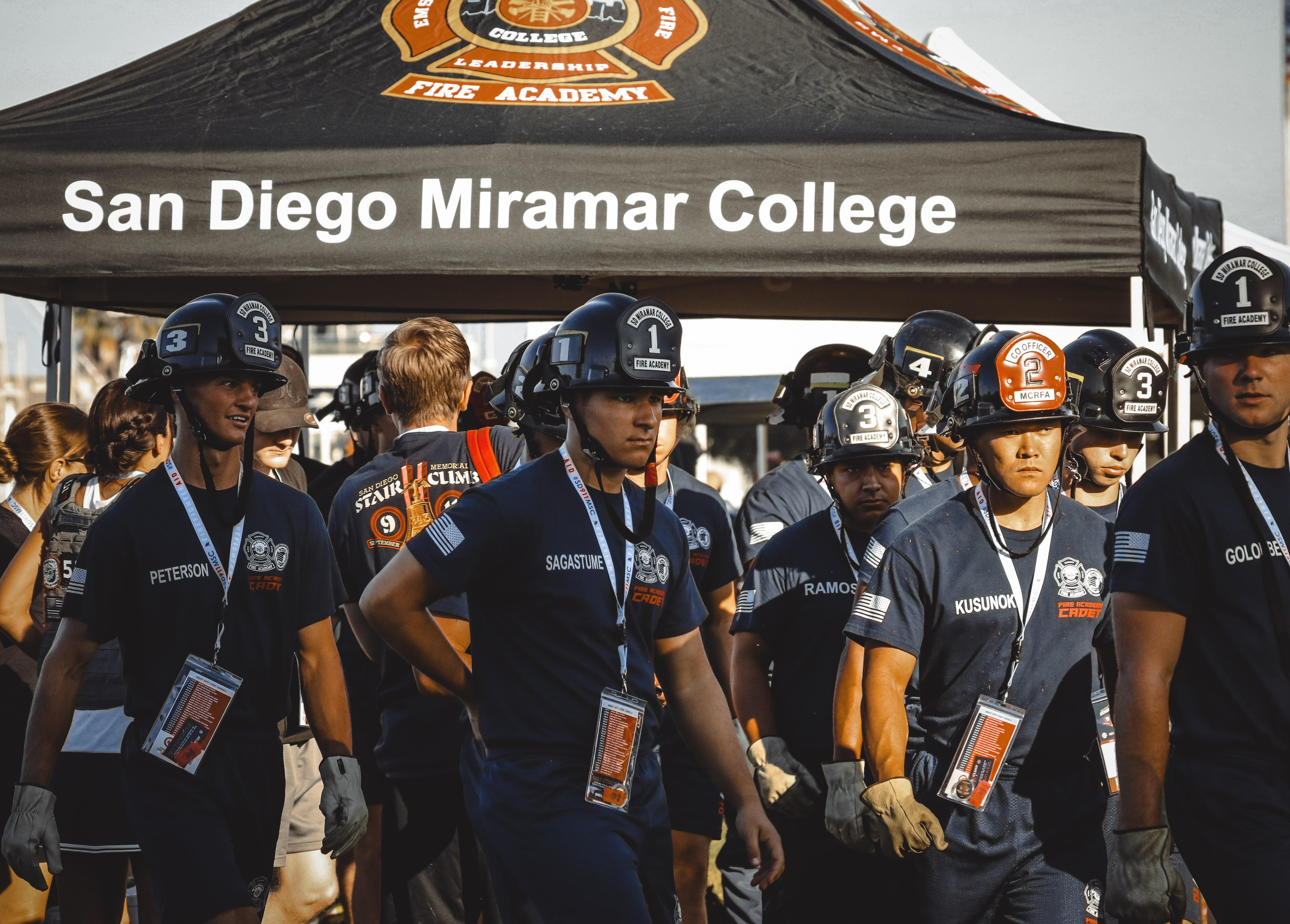 
Cadets in dark blue fire academy t-shirts and black fire helmets near the Miramar tent.&nbsp;
