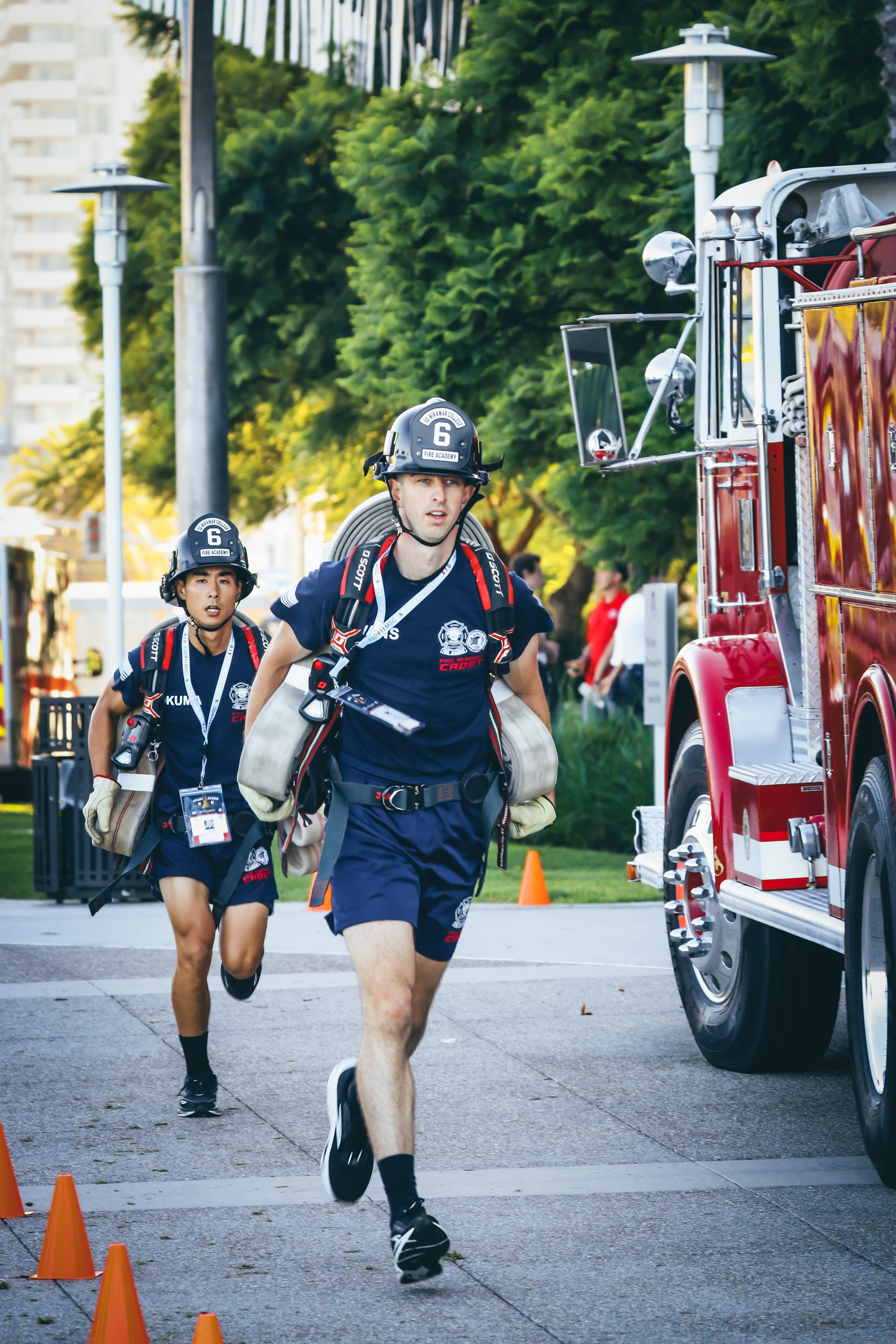 
Two cadets in blue t-shirts and shorts and black fire helmets carry their fire gear in the stair climb.&nbsp;
