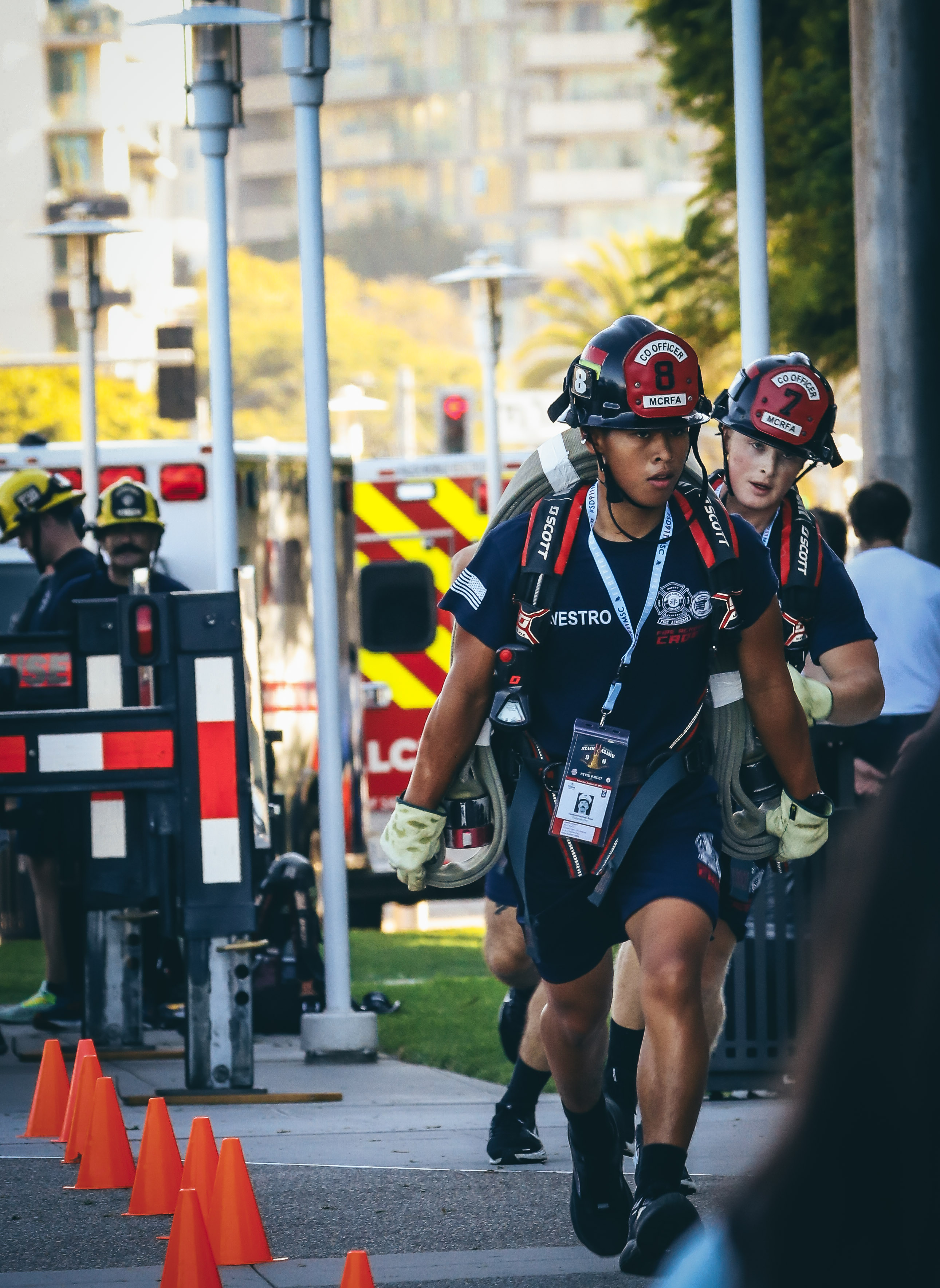 
Two cadets in blue t-shirts and shorts and black fire helmets carry their fire gear in the stair climb.&nbsp;
