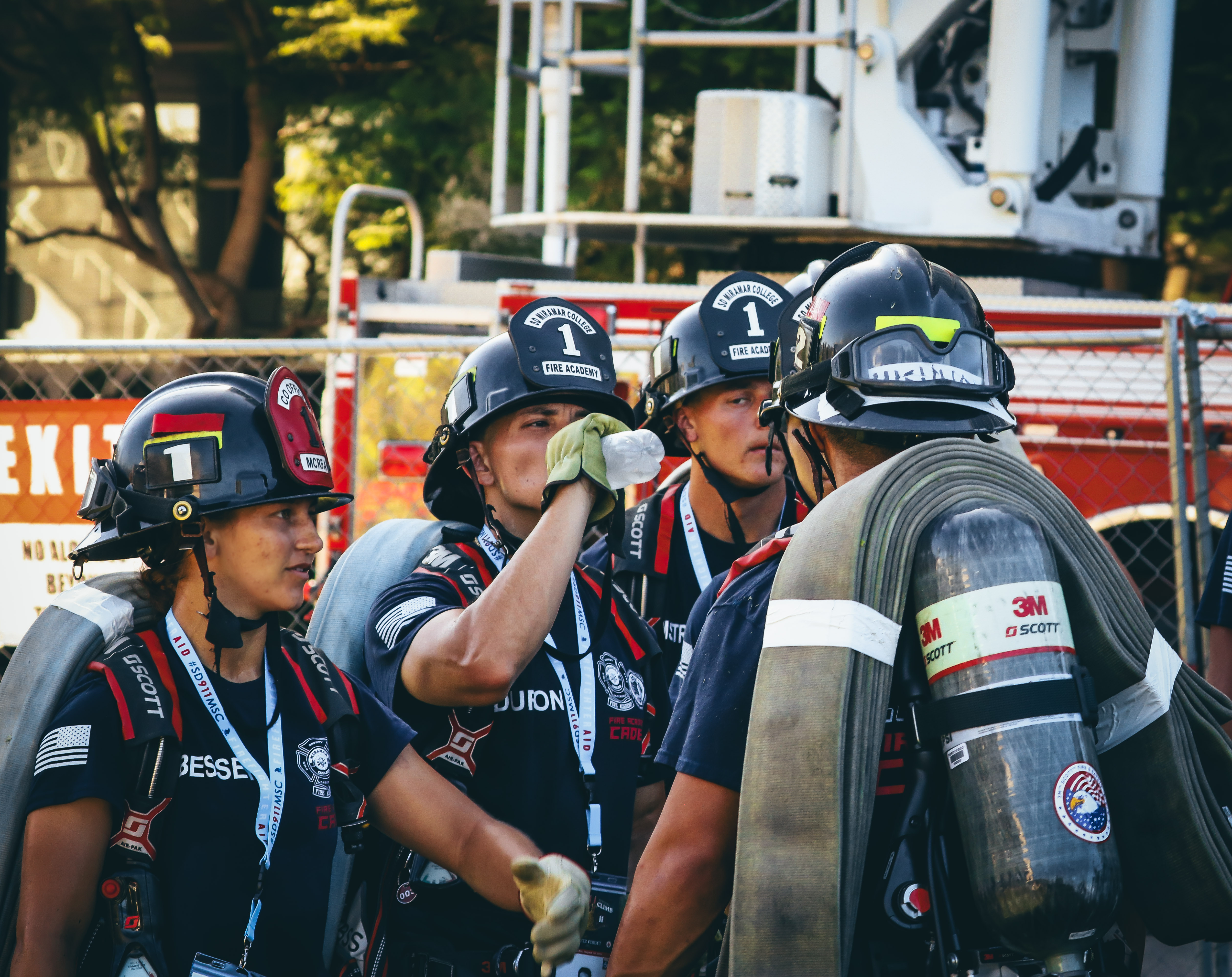 
Four cadets wearing fire helmets and holding their gear take a water break.
