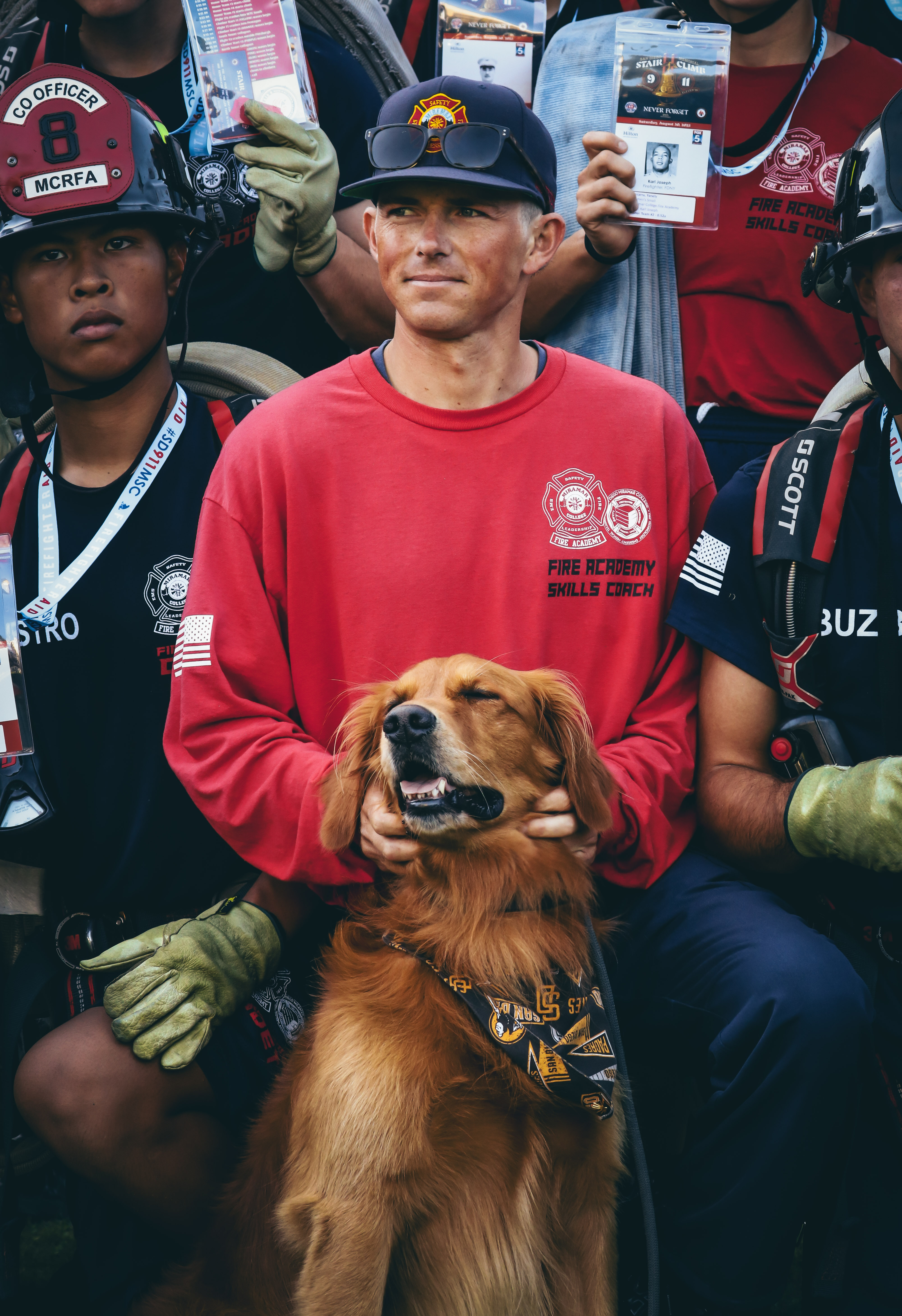 
A man in a red shirt with a golden retriever surrounded by Miramar cadets.
