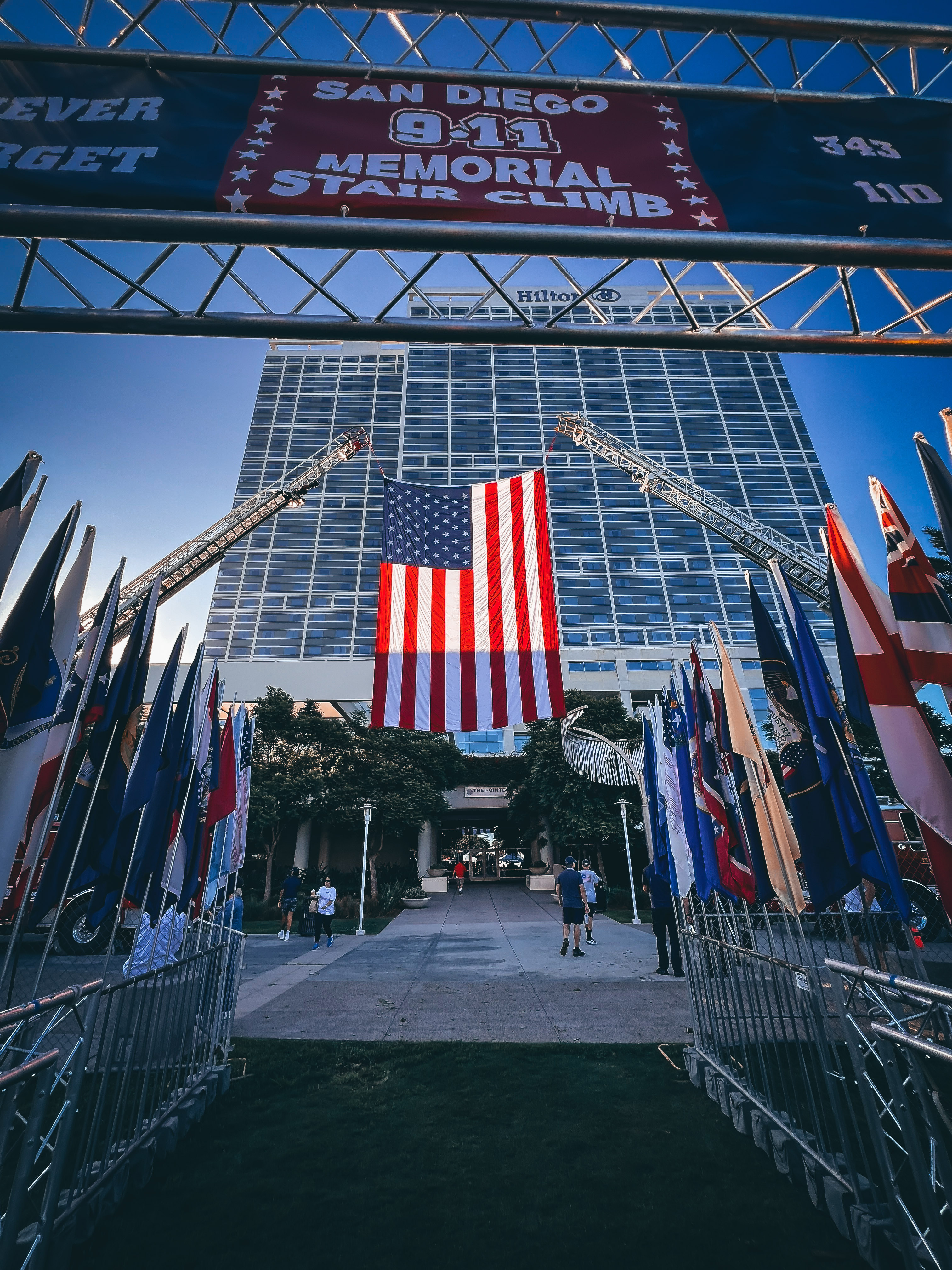 
An American flag is held up by two fire truck ladders at the entrance of the stair climb.
