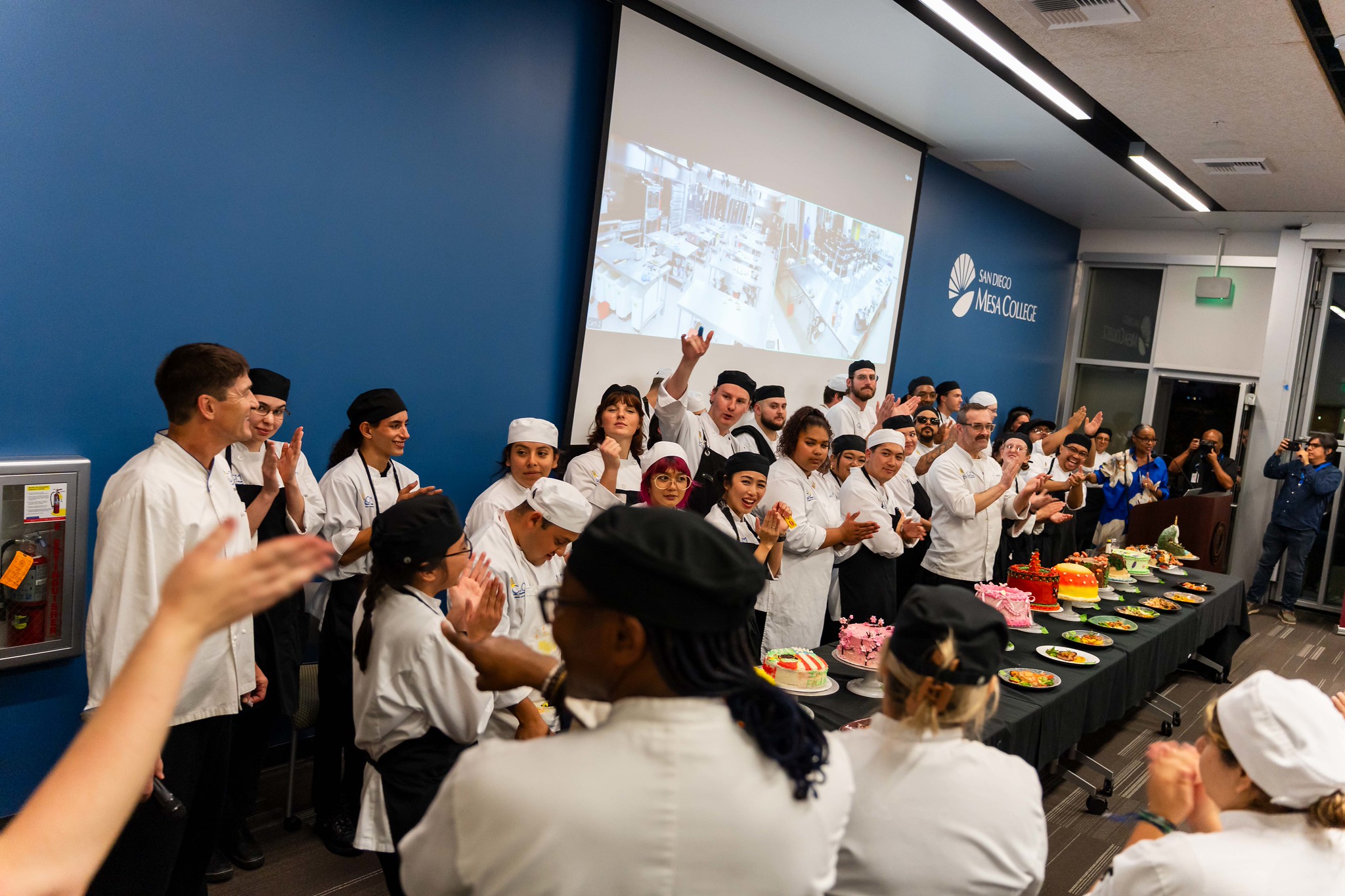 
A row of chefs line up with their cakes. 
