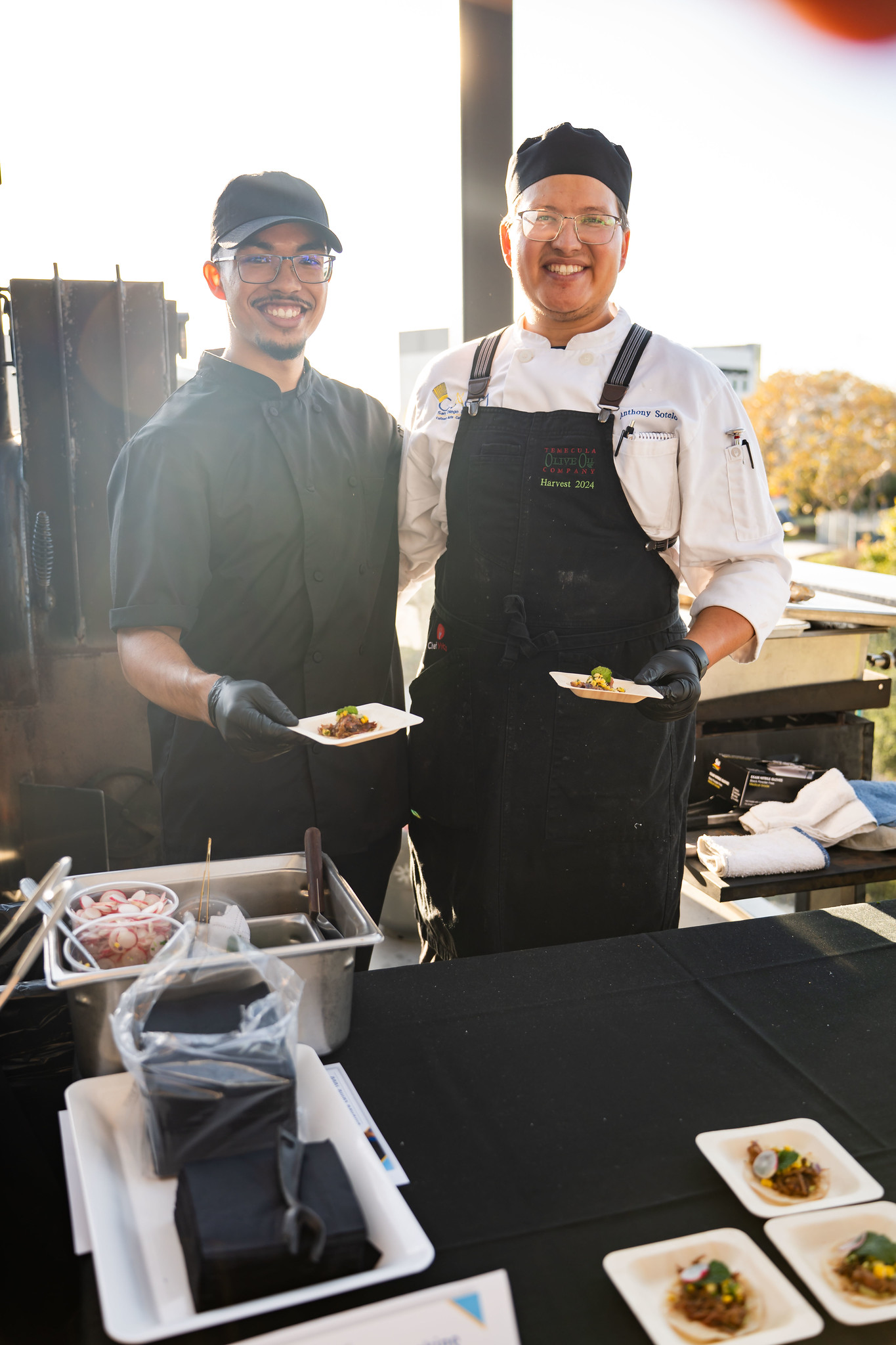 
Two chefs hold up tasting samples. 

