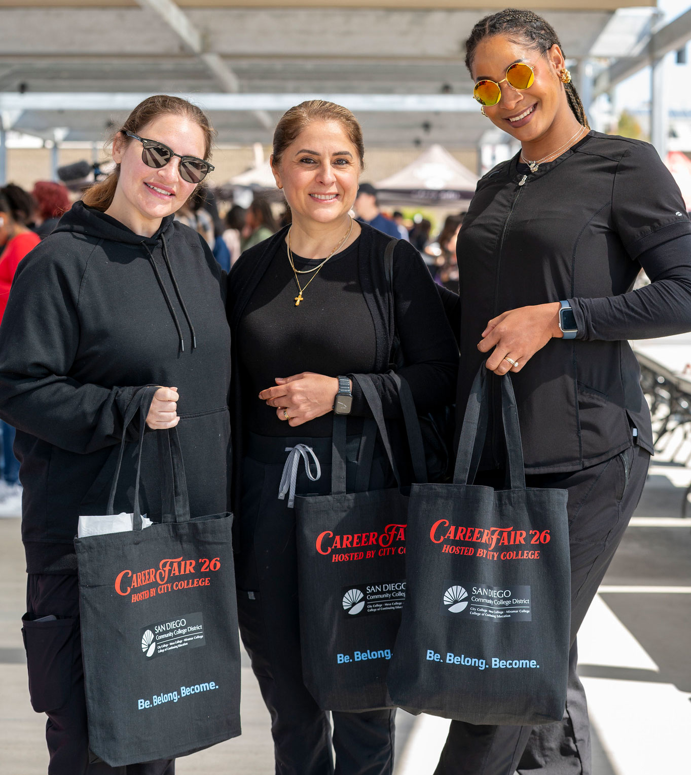 Three ladies hold up black canvas bags that say Career Fair 2026 in red.
