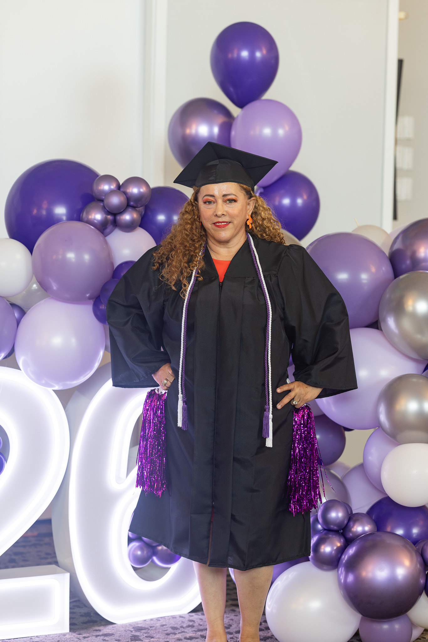 A graduate in front of a lit up 2026 and balloons.