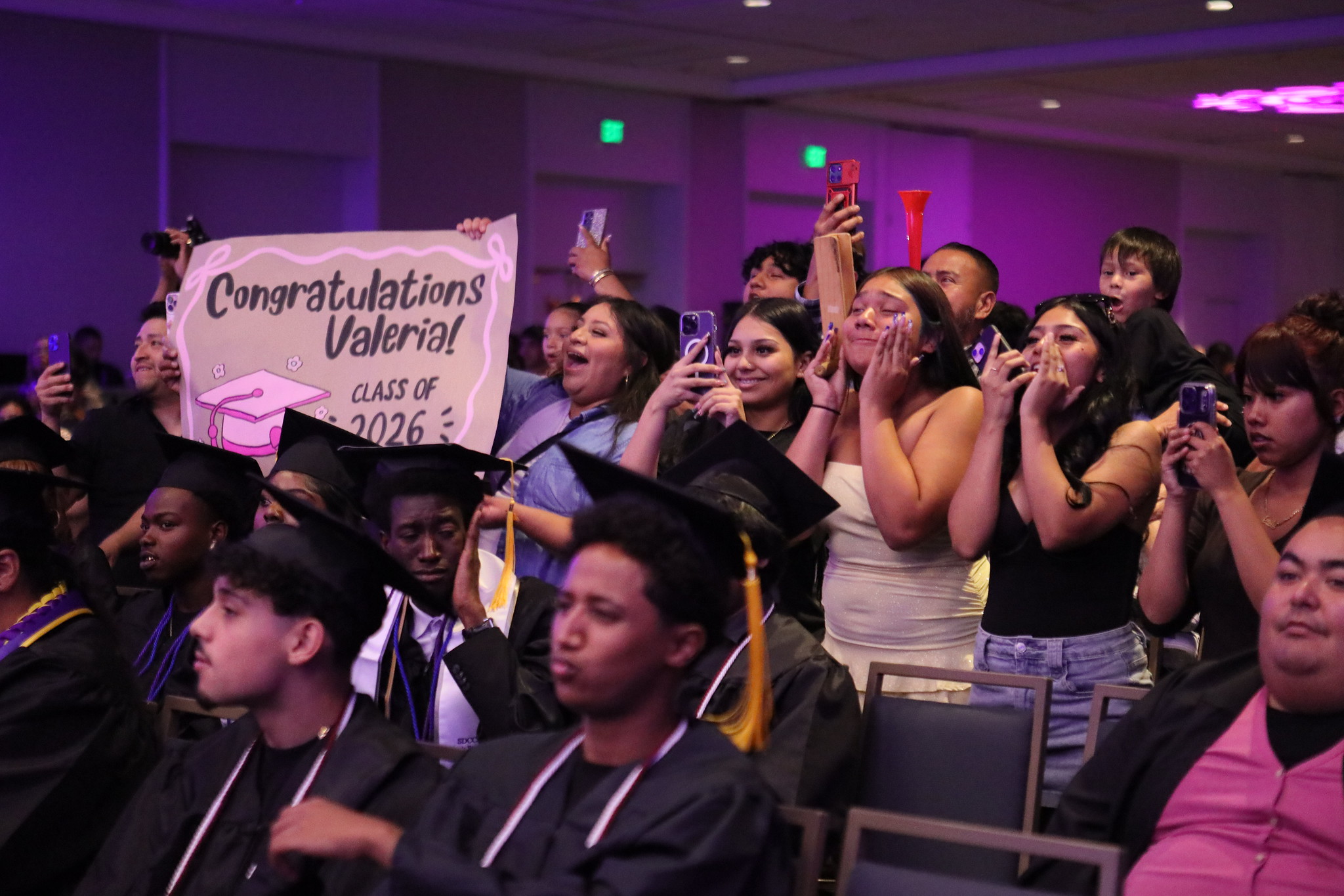 A group of family members stand and cheer A sign says Congratulations Valeria.