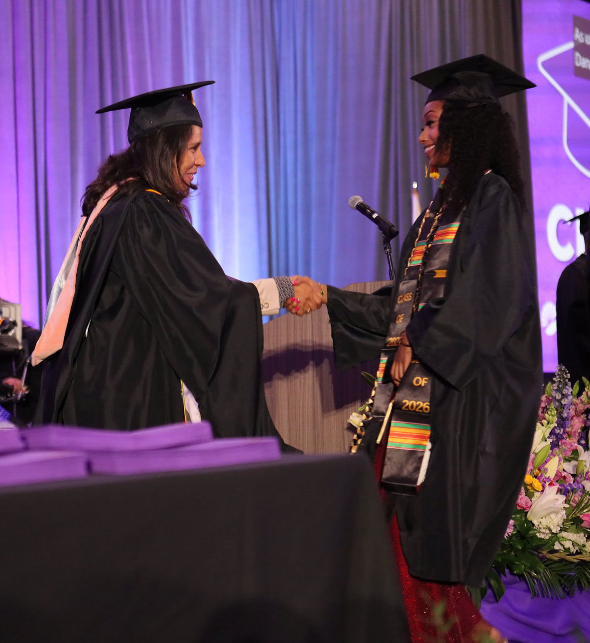 Trustess Geysil Arroyo shakes a graduate's hand.