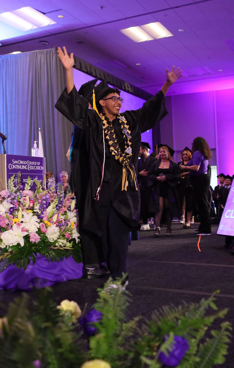 A grad waves to the audience from the stage.