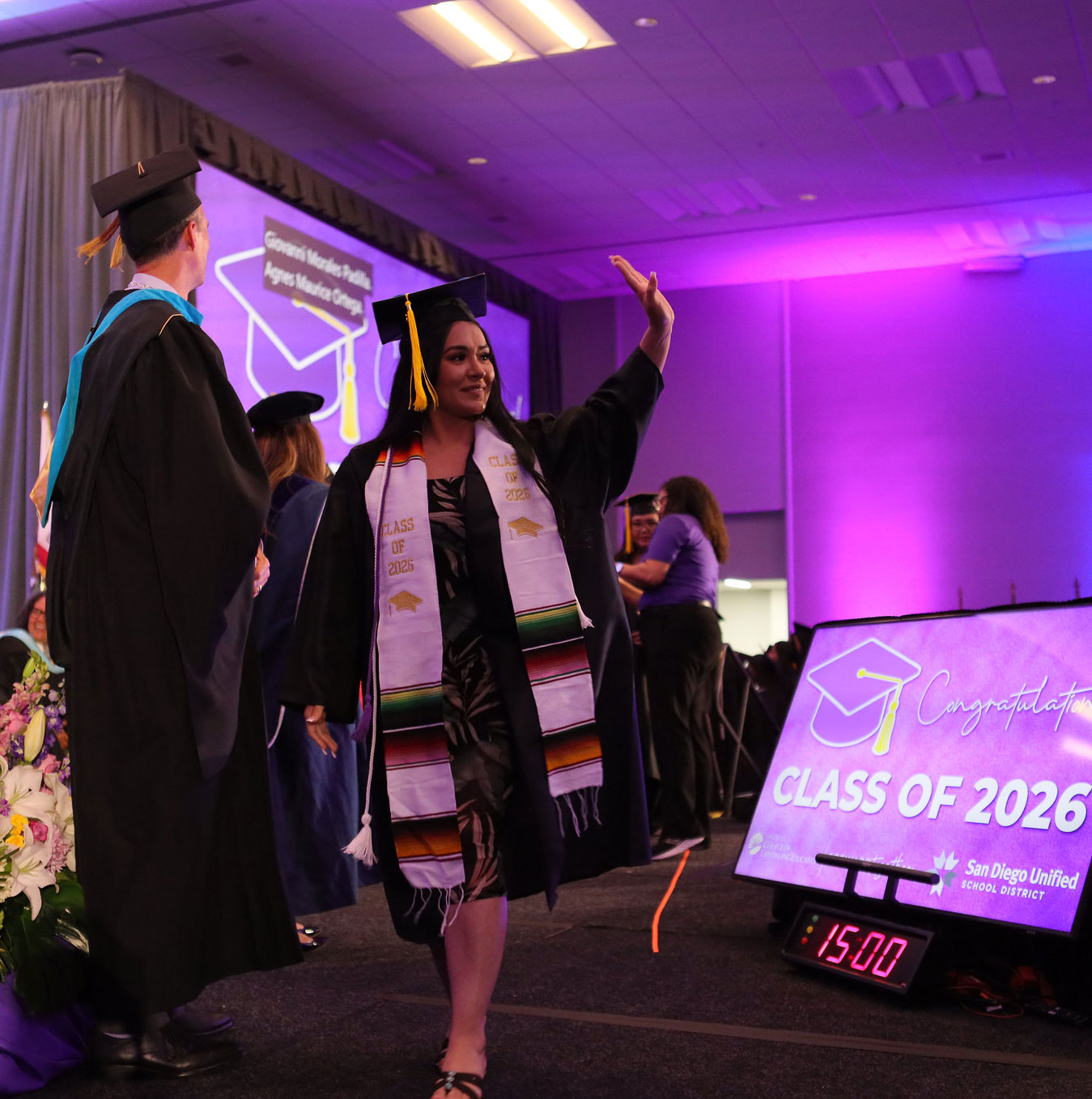 A grad waves to the audience from the stage.